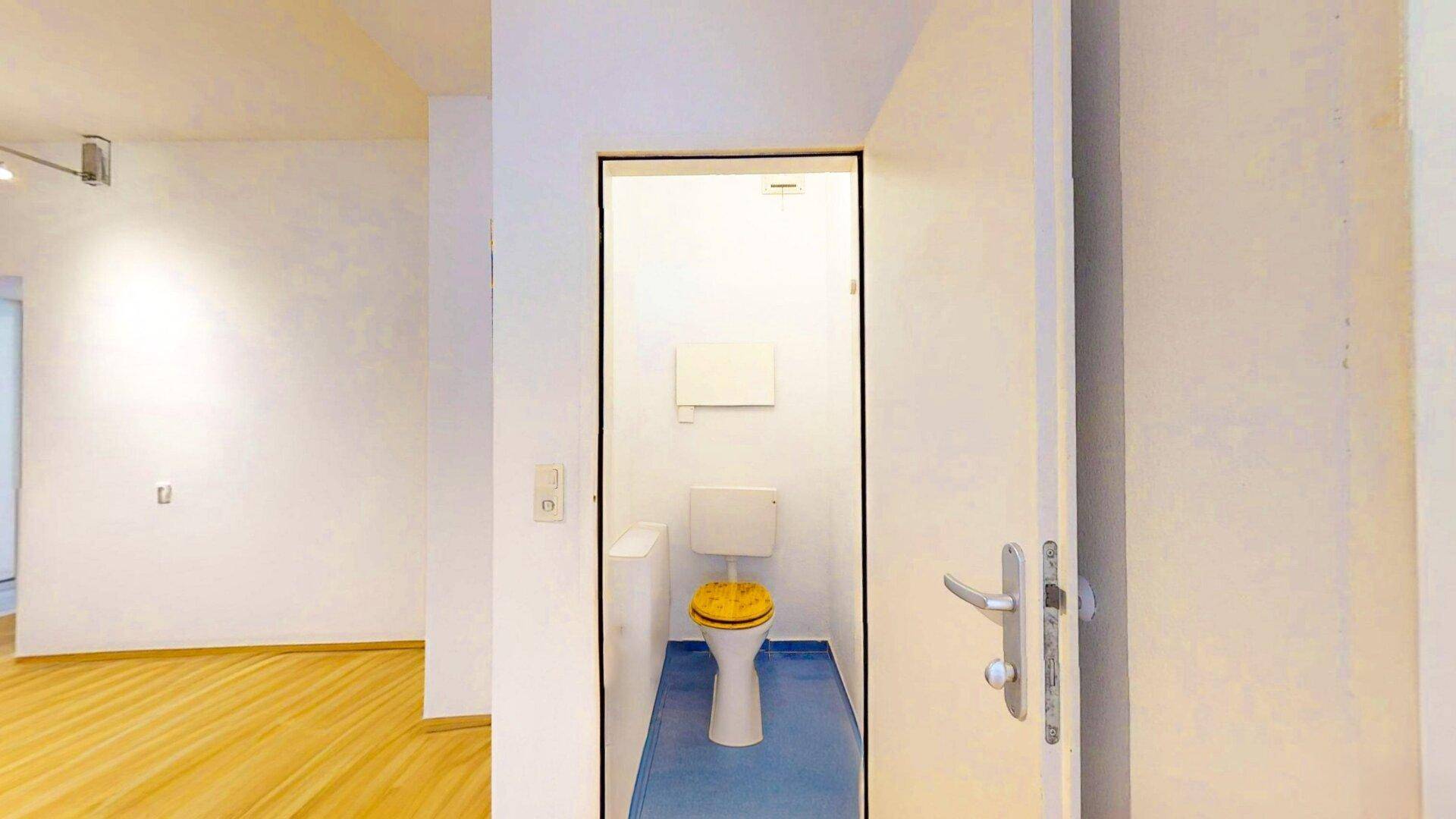 Separates WC mit gelbem Toilettensitz und blauen Bodenfliesen, einfach und funktional.