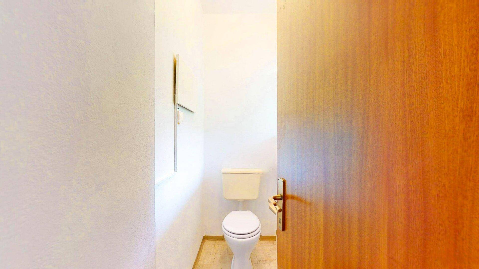 Kleines, separates WC mit einfacher Toilette und weiß gefliesten Wänden, funktional und sauber.