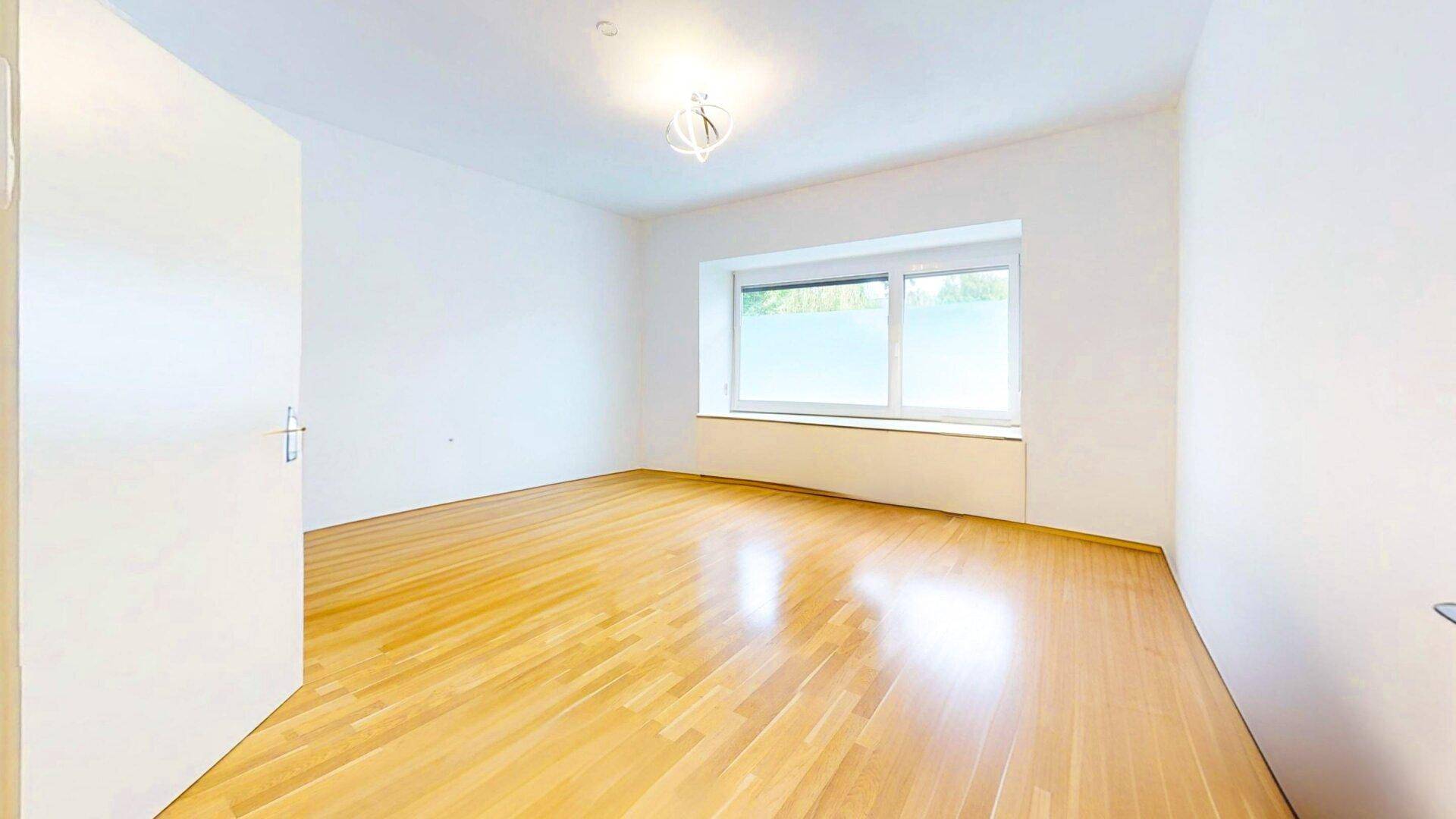 Helles Zimmer mit großem Fenster, Holzparkettboden und weißen Wänden, bietet viel Tageslicht.