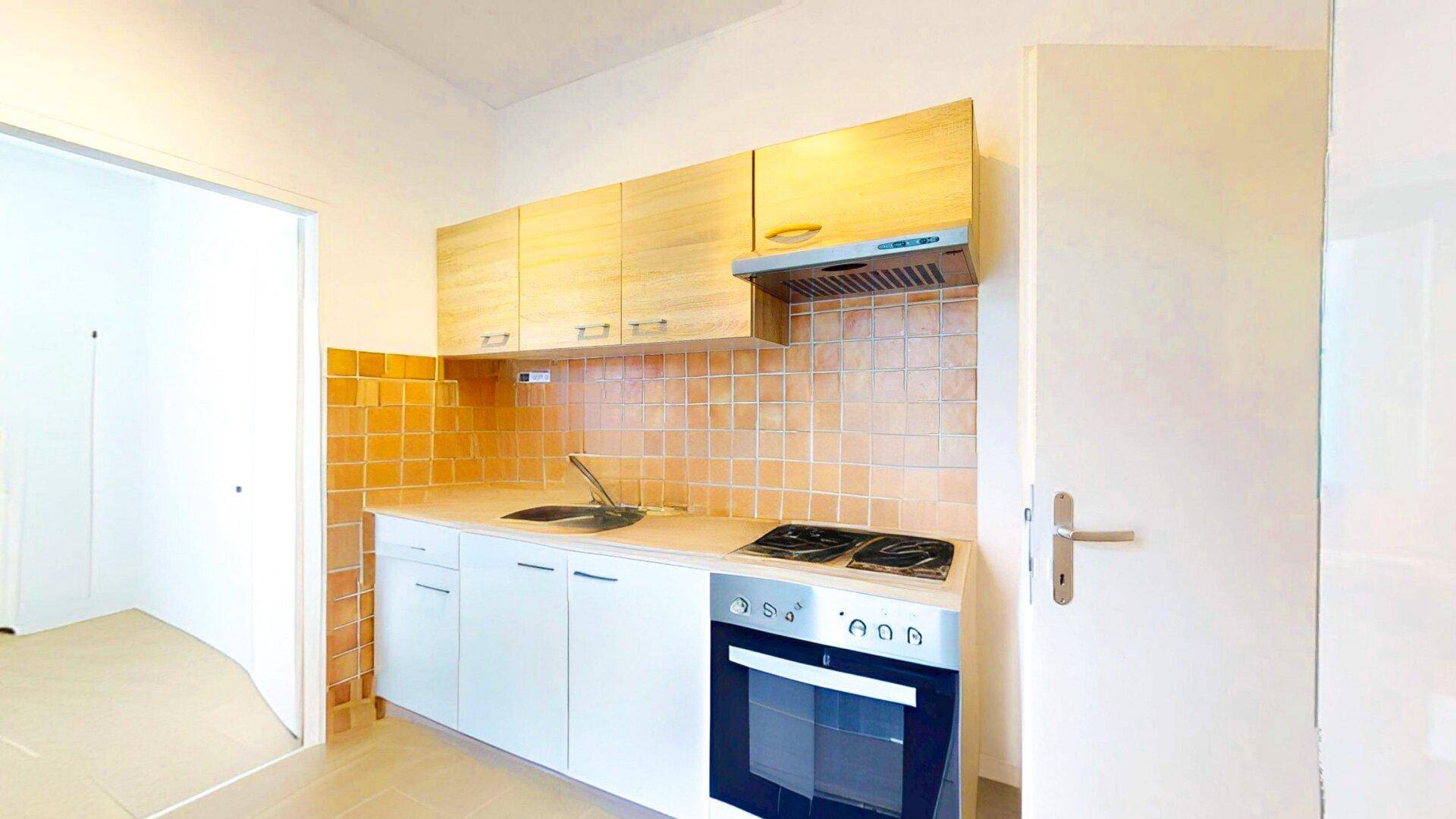 Kleine Küche mit Holzschränken, Herd und Backofen, sowie orangefarbenen Fliesen als Spritzschutz.