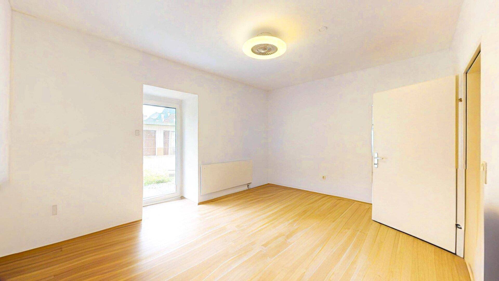 Helles Zimmer mit Zugang nach draußen, Holzparkettboden und weißen Wänden, vielseitig nutzbar.