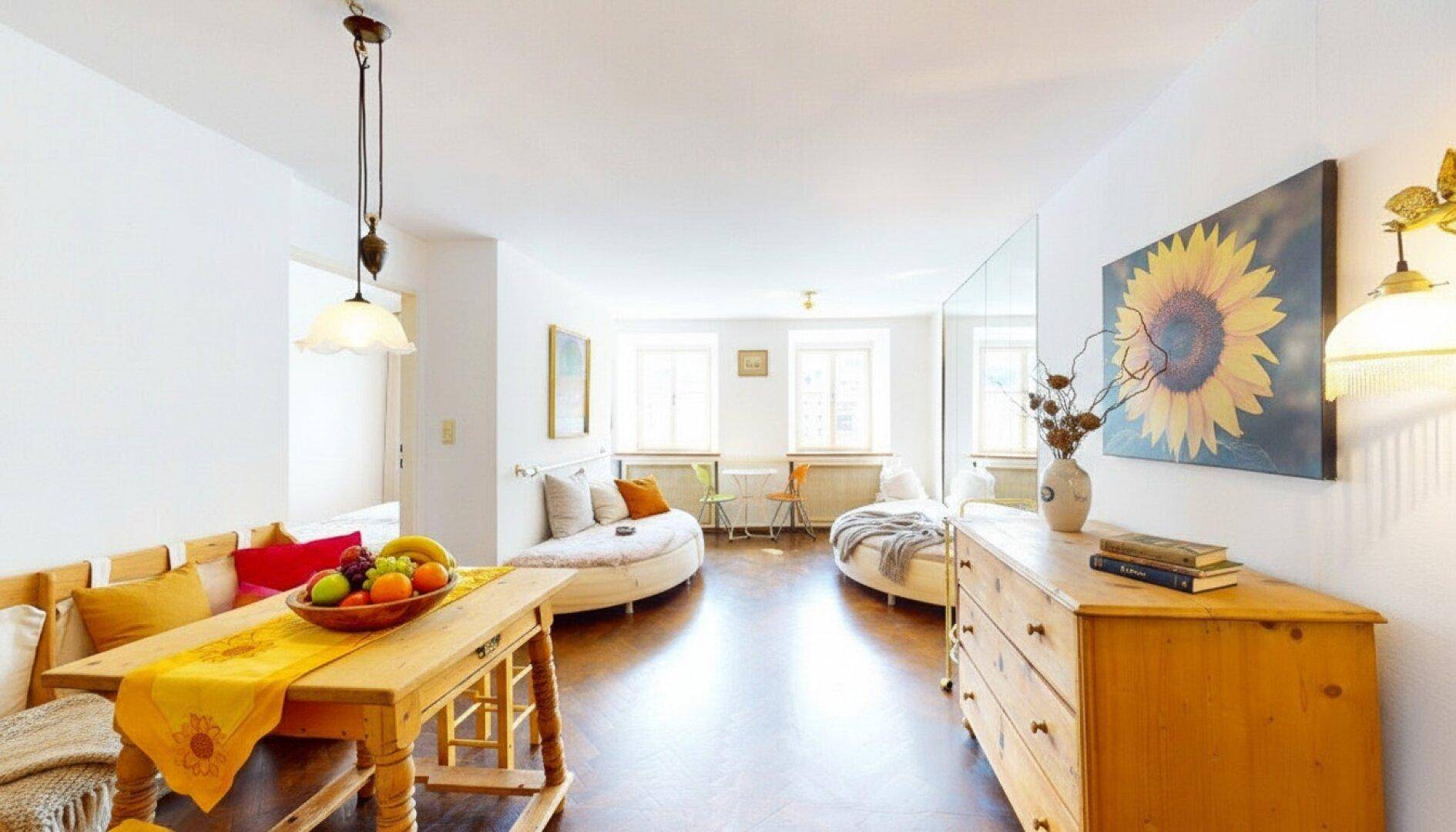 Heller Wohn- und Essbereich mit Holztisch, Sitzbank und zwei runden Sofas.