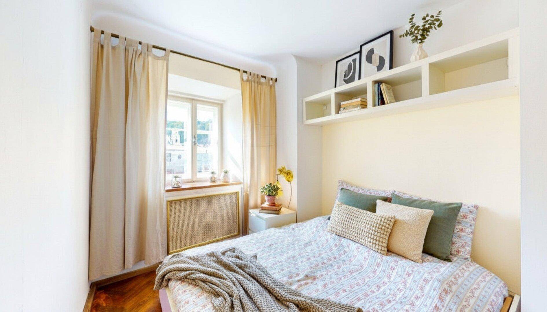 Helles Schlafzimmer mit Doppelbett, Nachttisch und Fenster mit Vorhängen.