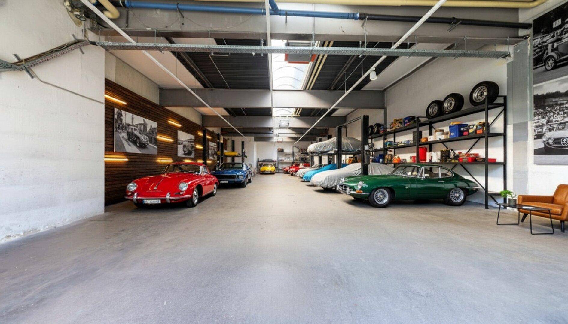 Geräumige Halle, eingerichtet als Oldtimer-Lager mit Regalen, Sitzgelegenheiten und mehreren klassischen Fahrzeugen.