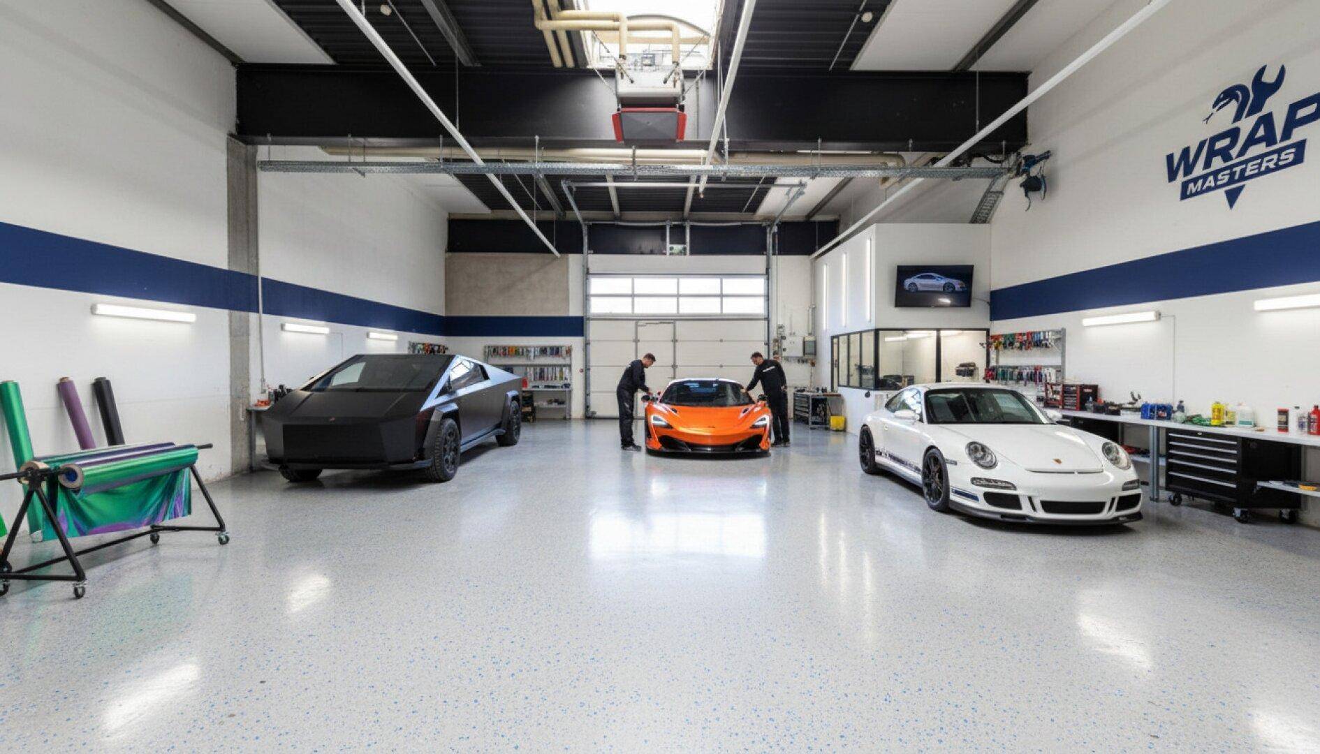 Moderne Werkstatt für Fahrzeugfolierung mit mehreren Luxusautos, speziellen Werkzeugen und einem sauberen, gesprenkelten Boden.