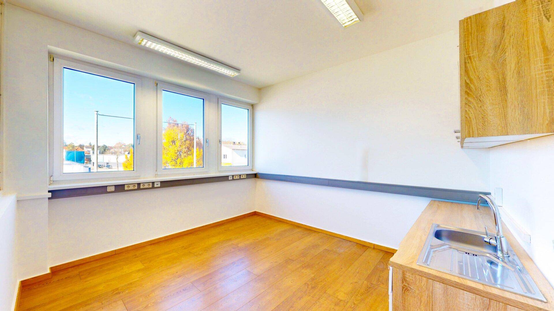 Kleine Küchenzeile mit Spüle und Holzschränken in einem hellen Raum mit großen Fenstern und Ausblick.