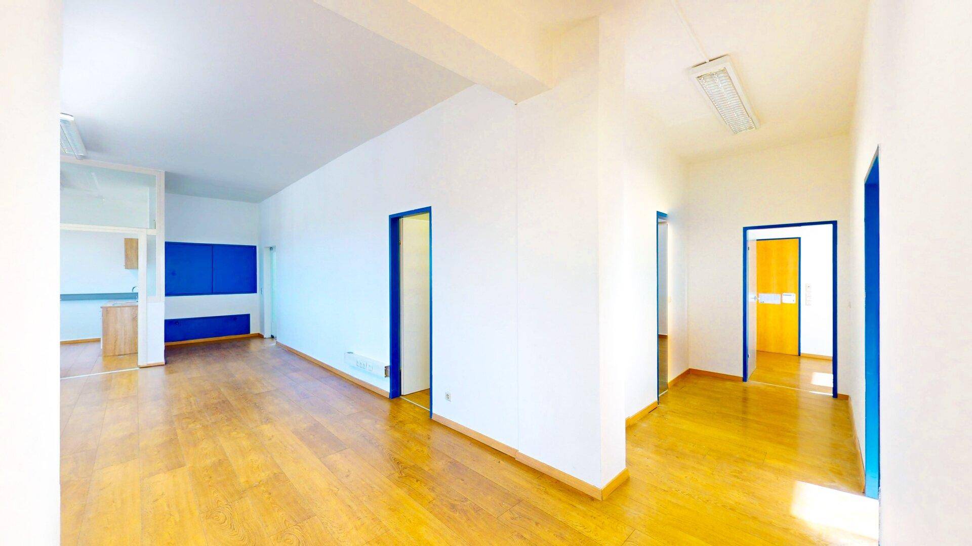 Langer Flur mit hellem Holzfußboden und mehreren Türen, die zu verschiedenen Büroräumen führen, mit blauen Akzenten.