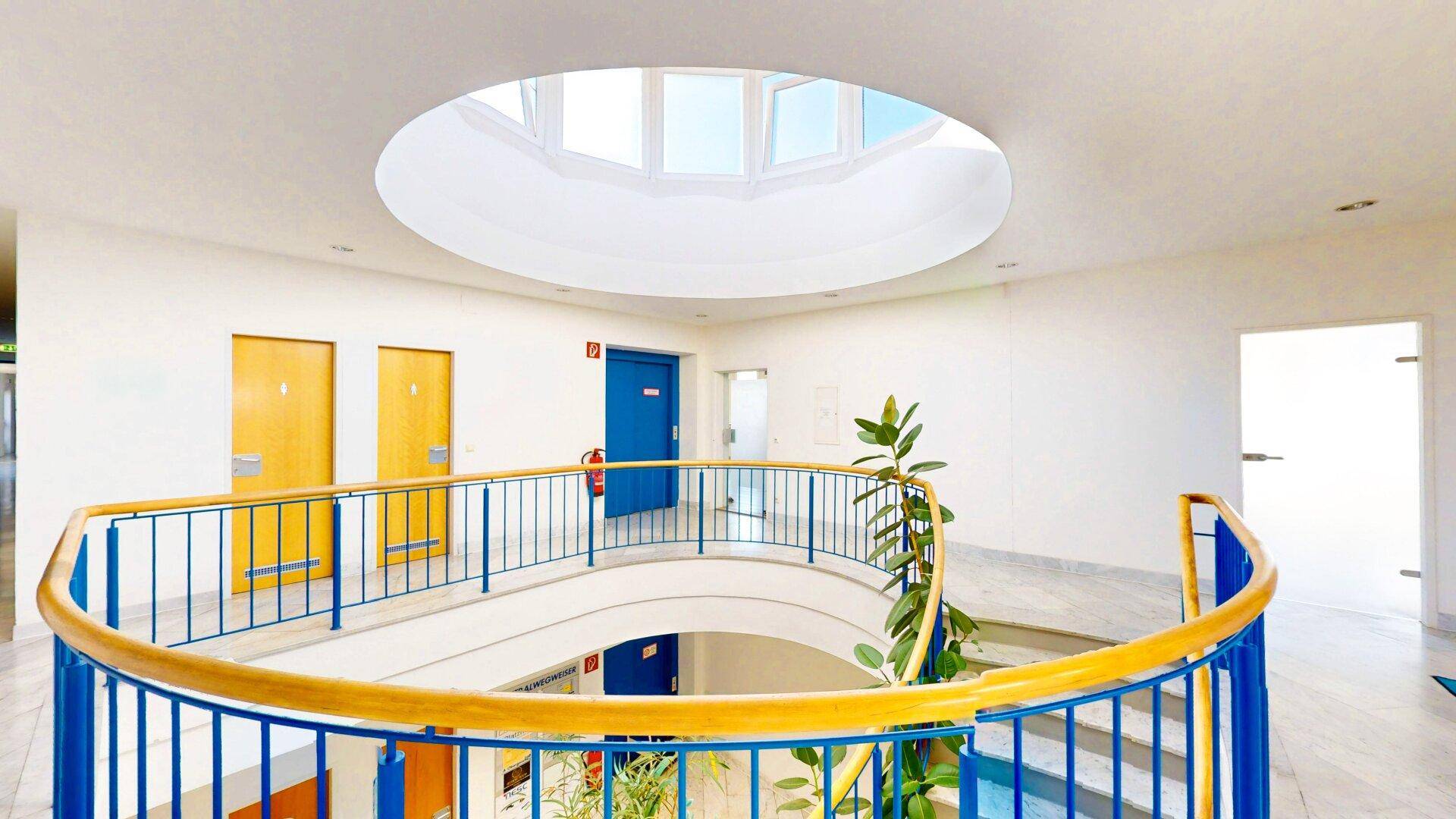 Großzügiges Treppenhaus mit runder Treppe, Oberlicht und Marmorboden, hell und einladend gestaltet.