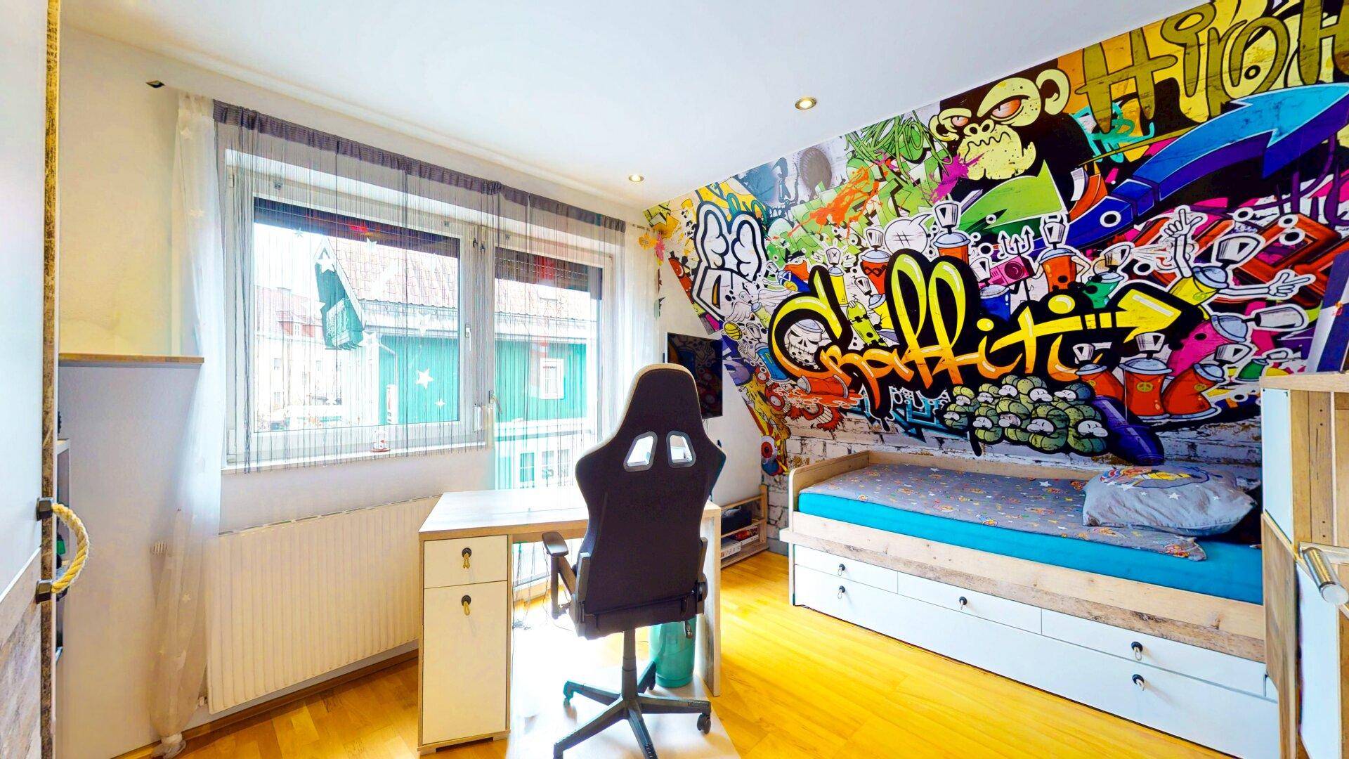 Kinderzimmer mit farbenfroher Graffiti-Tapete, Schreibtisch und einem Bett mit Stauraum.