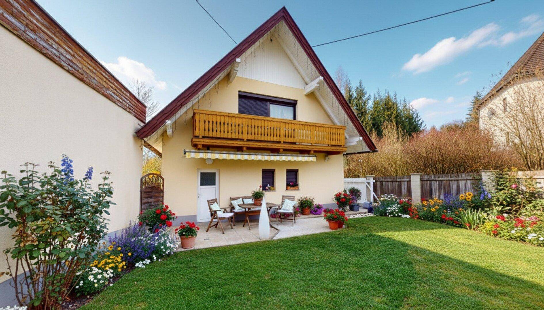 Rückseite des Hauses mit gepflegtem Garten, möblierter Terrasse und einem Balkon im Obergeschoss.