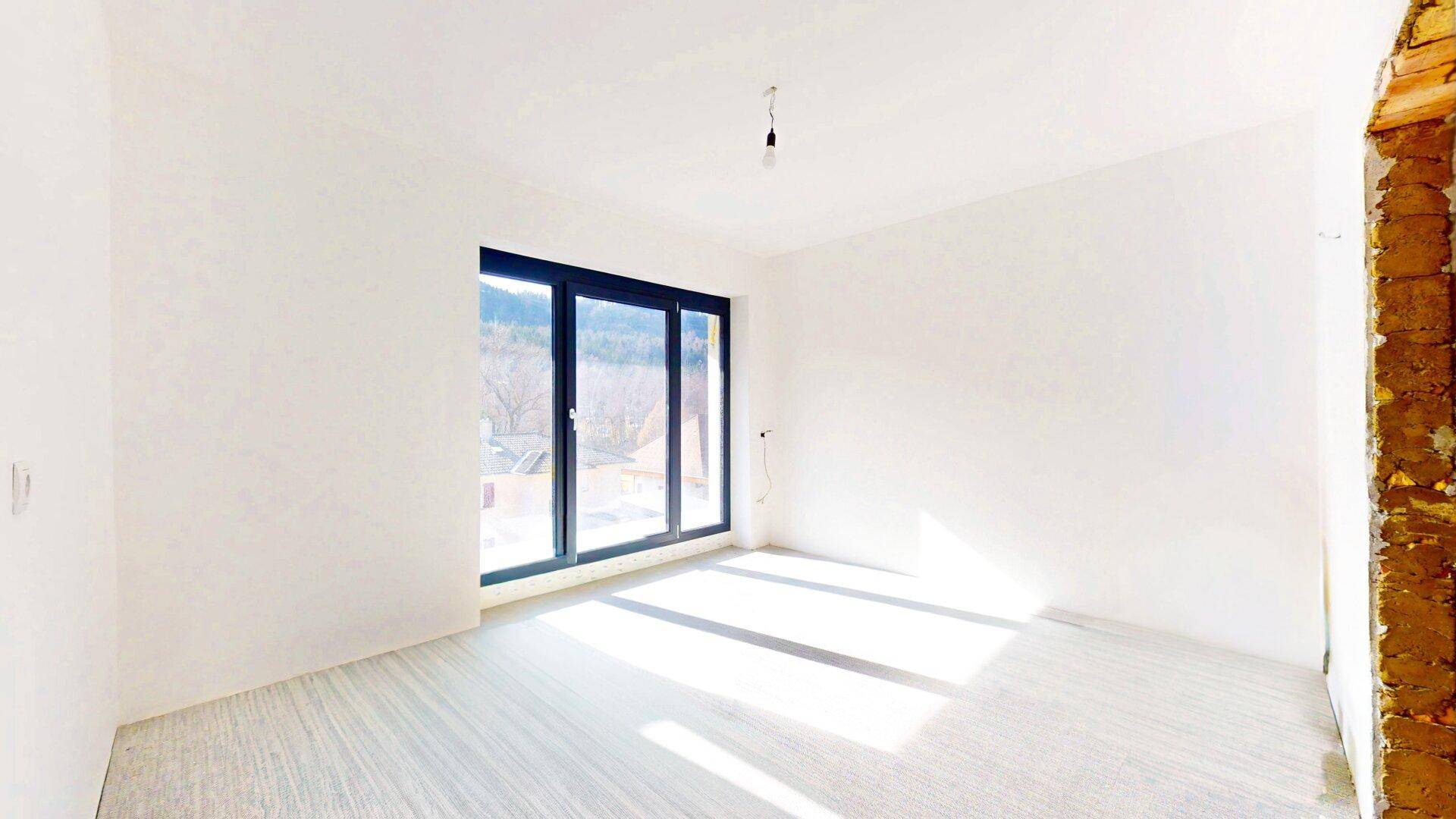 Lichtdurchflutetes Zimmer mit großen Fenstern und Blick ins Grüne, bereit für individuelle Gestaltung.