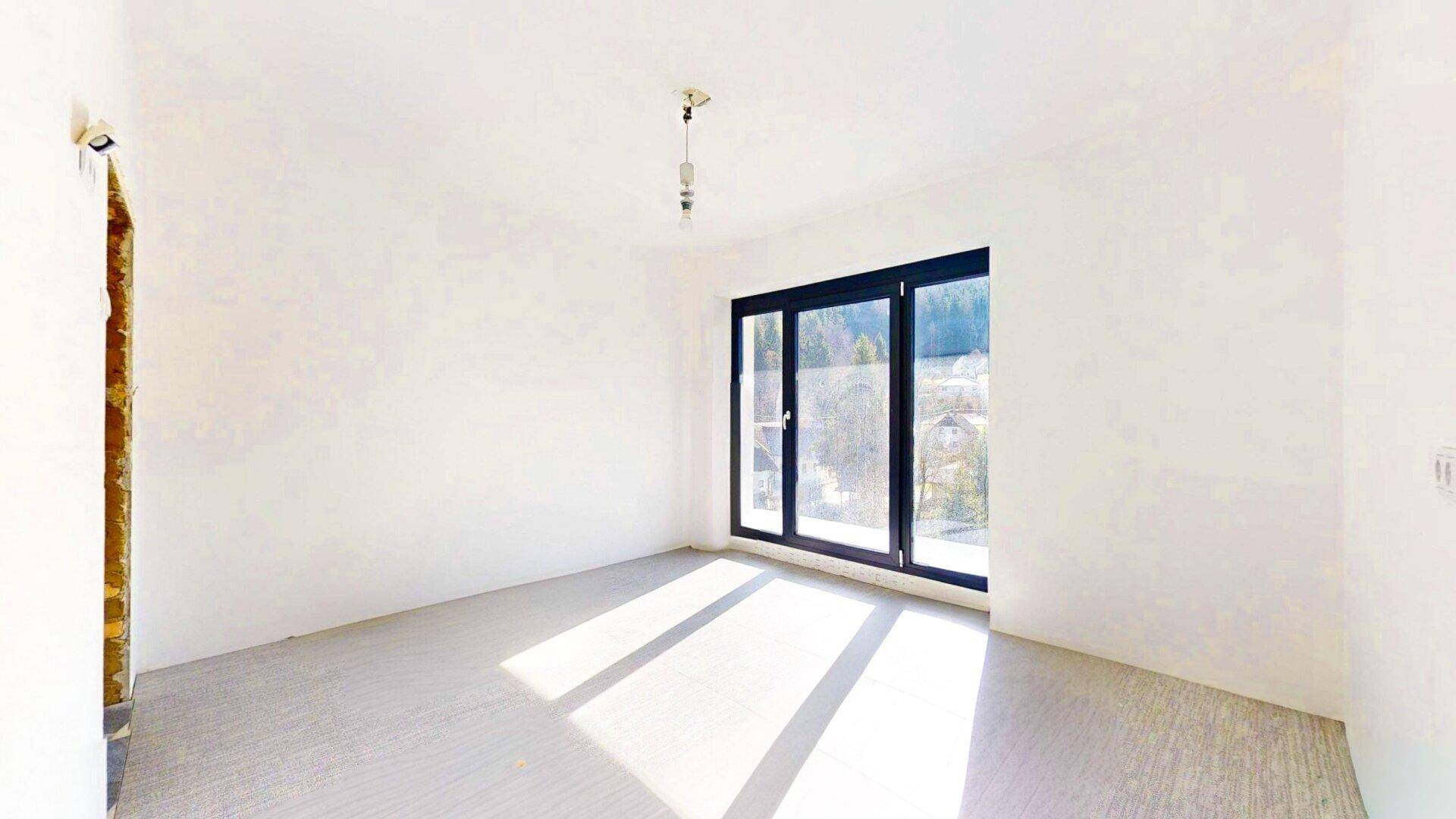 Geräumiger, heller Raum mit großen Fenstern und Blick auf die umliegende Natur, ideal als Wohnzimmer.