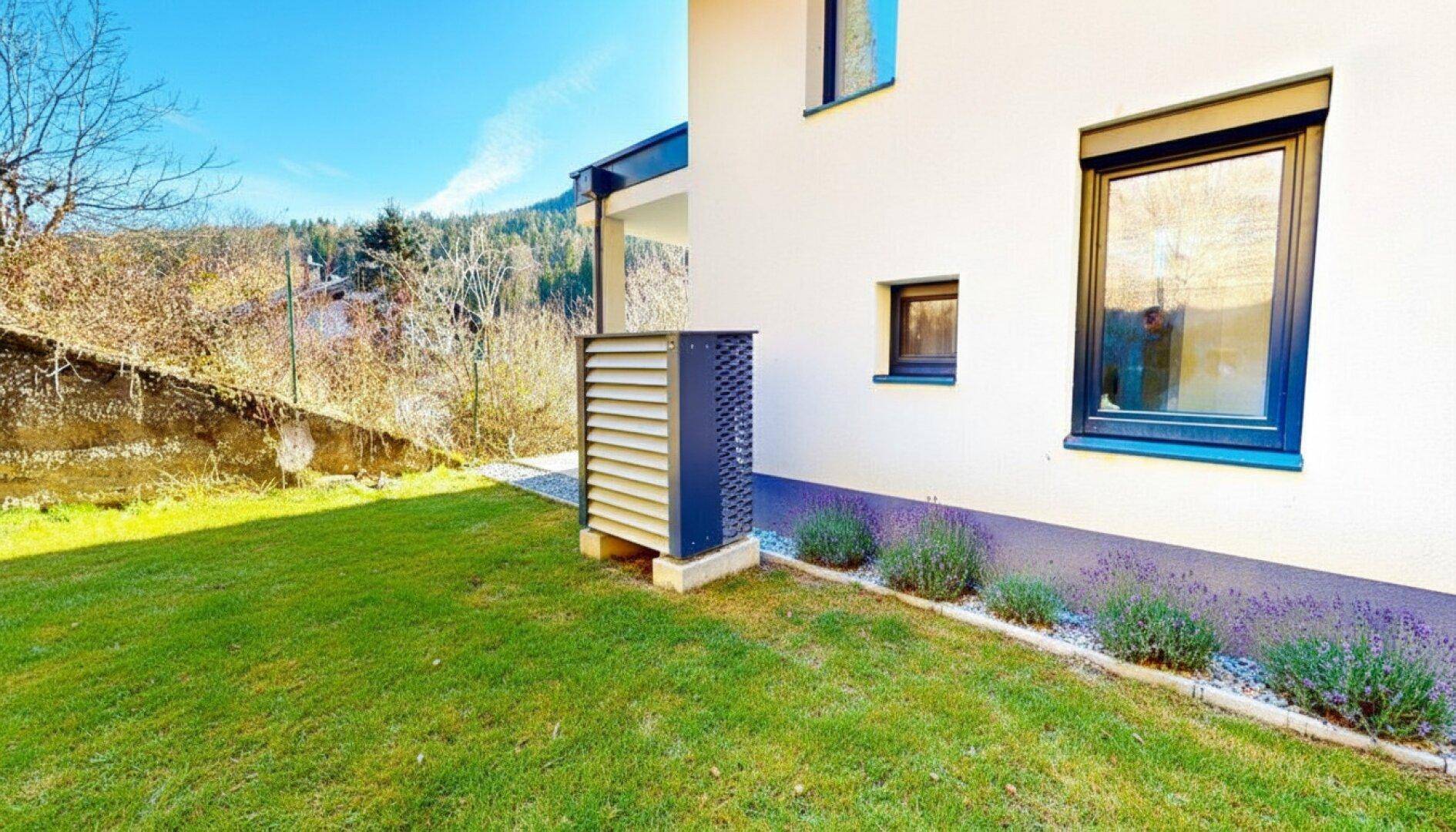 Kleiner Rasenbereich neben dem Haus mit einer Wärmepumpe und dekorativen Pflanzen.