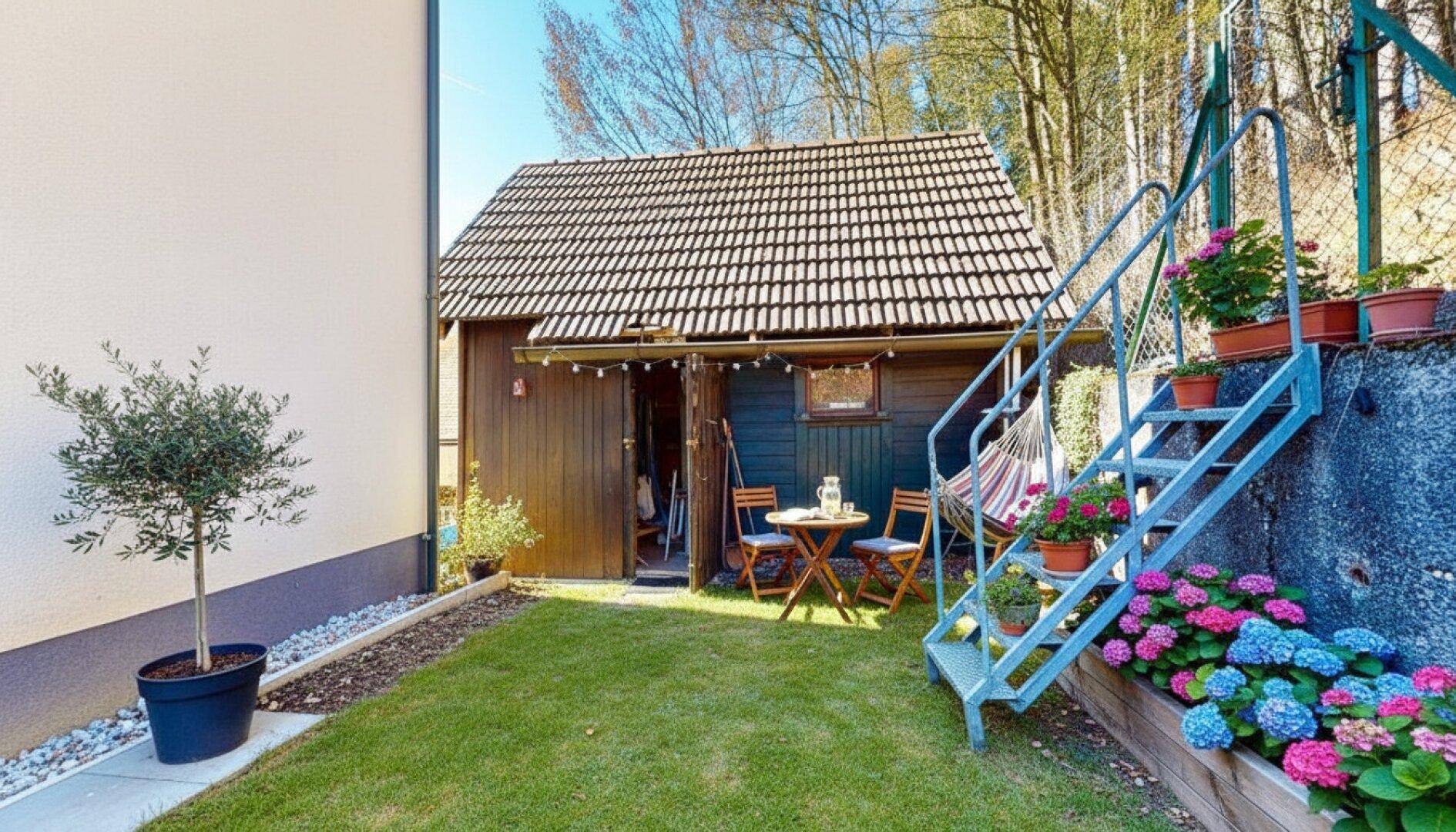 Gemütlicher Gartenbereich mit Gartenhaus, Sitzgelegenheiten und bunten Blumenbeeten.