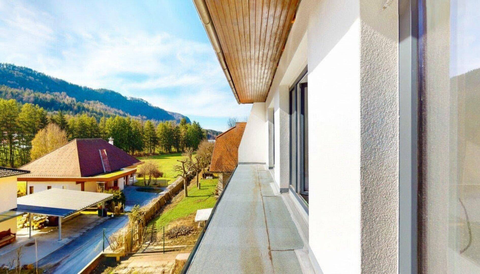 Schmaler Balkon mit Holzverkleidung und weitem Blick auf die grüne Landschaft und Nachbarhäuser.