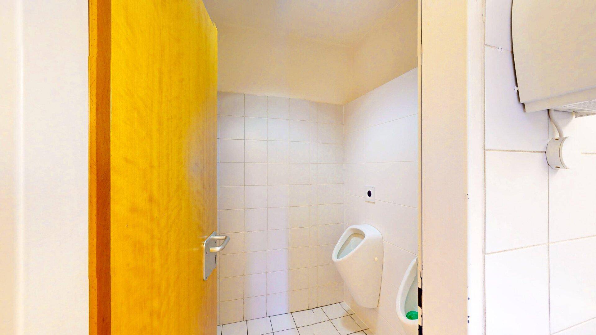 Sauberer Toilettenraum mit weißen Fliesen, Urinalen und einer gelben Holztür, praktisch und hygienisch.