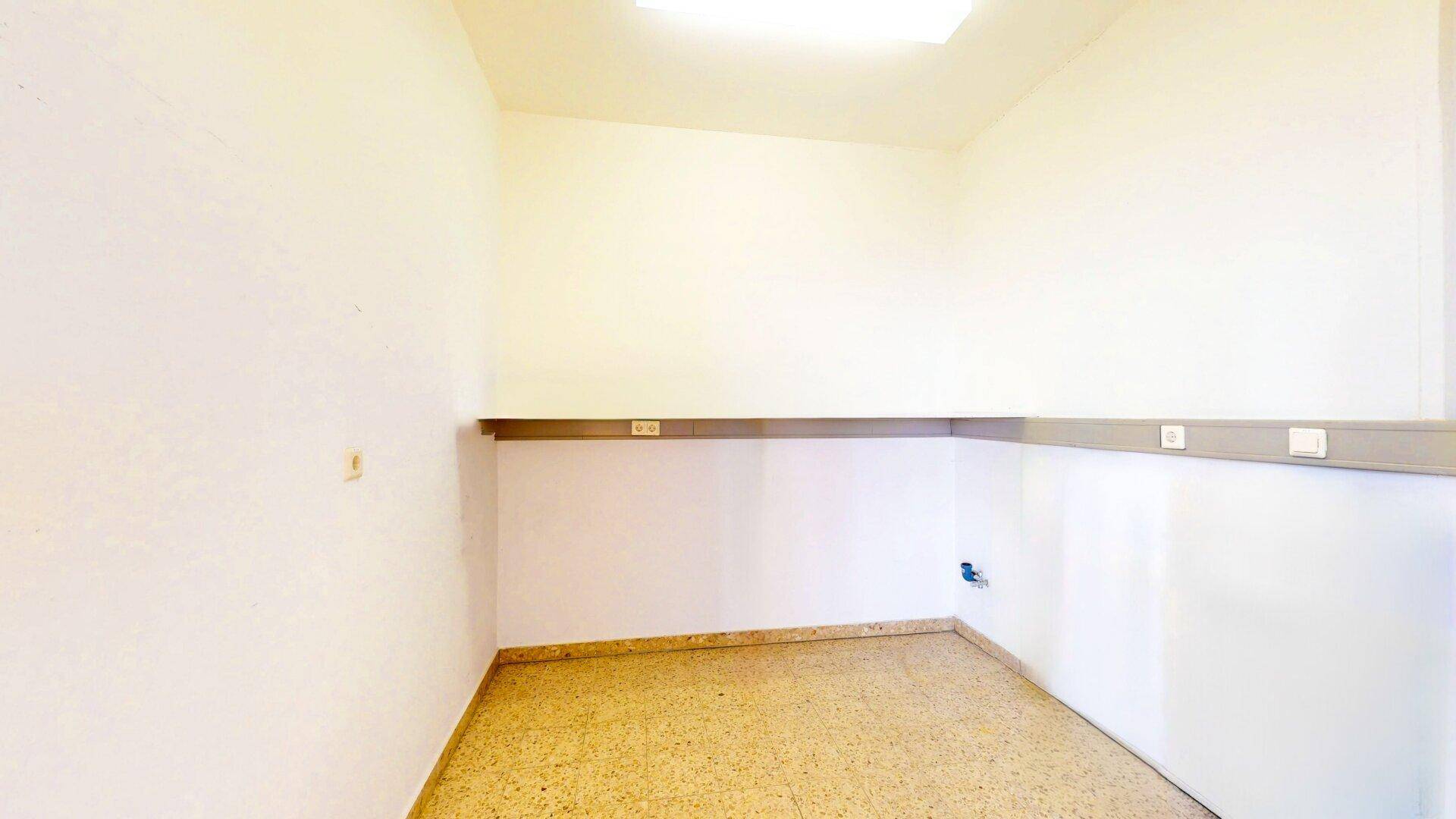 Kleiner, leerer Raum mit hellem Terrazzoboden und einer Ablagefläche an der Wand, ideal als Abstellraum.