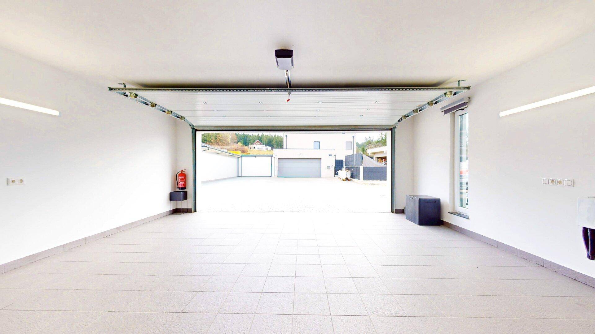 Geräumige Garage mit Fliesenboden und offenem Tor zur Einfahrt.