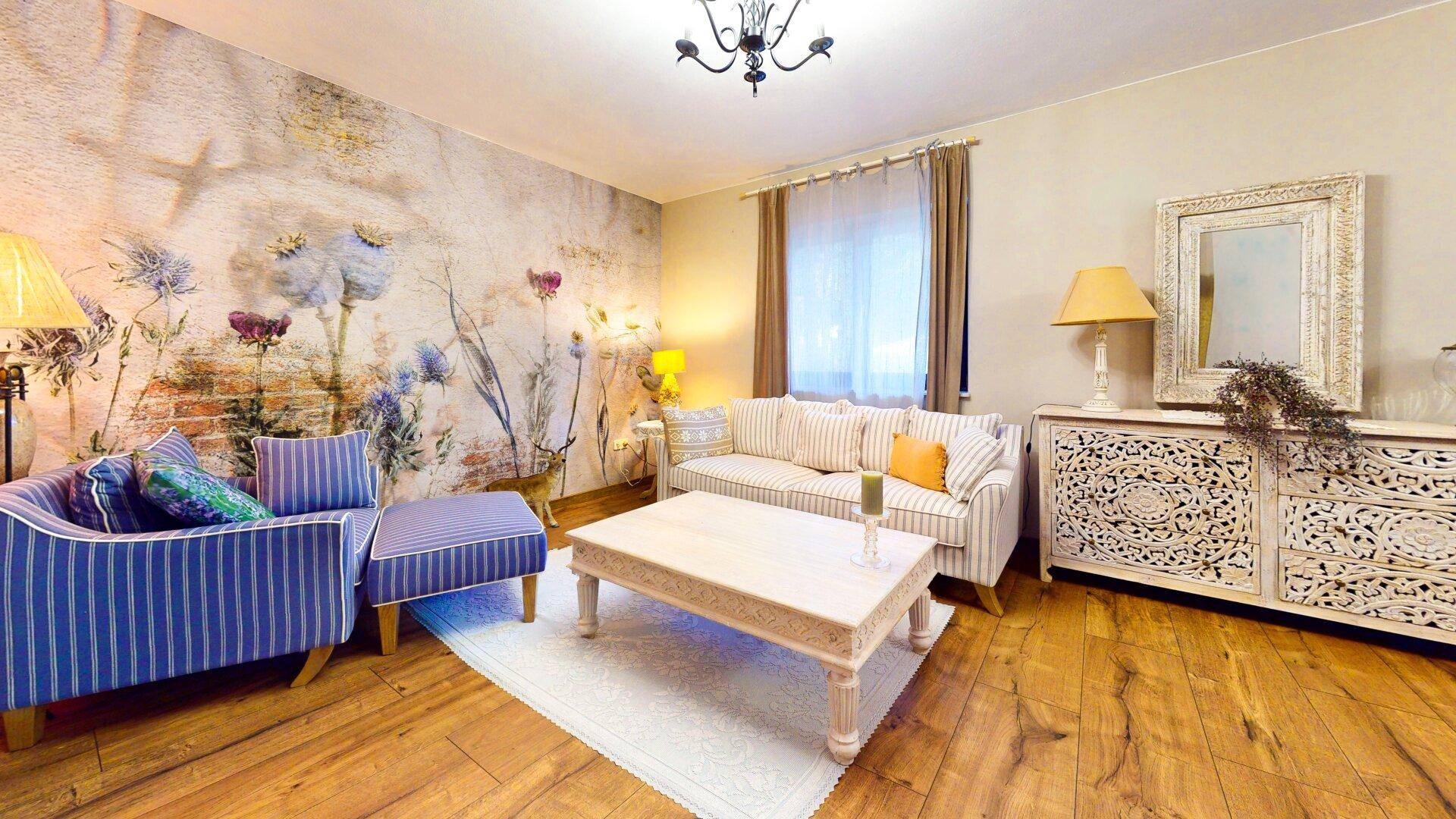 Helles Wohnzimmer mit gestreiftem Sofa, floraler Wandgestaltung und Holzboden.
