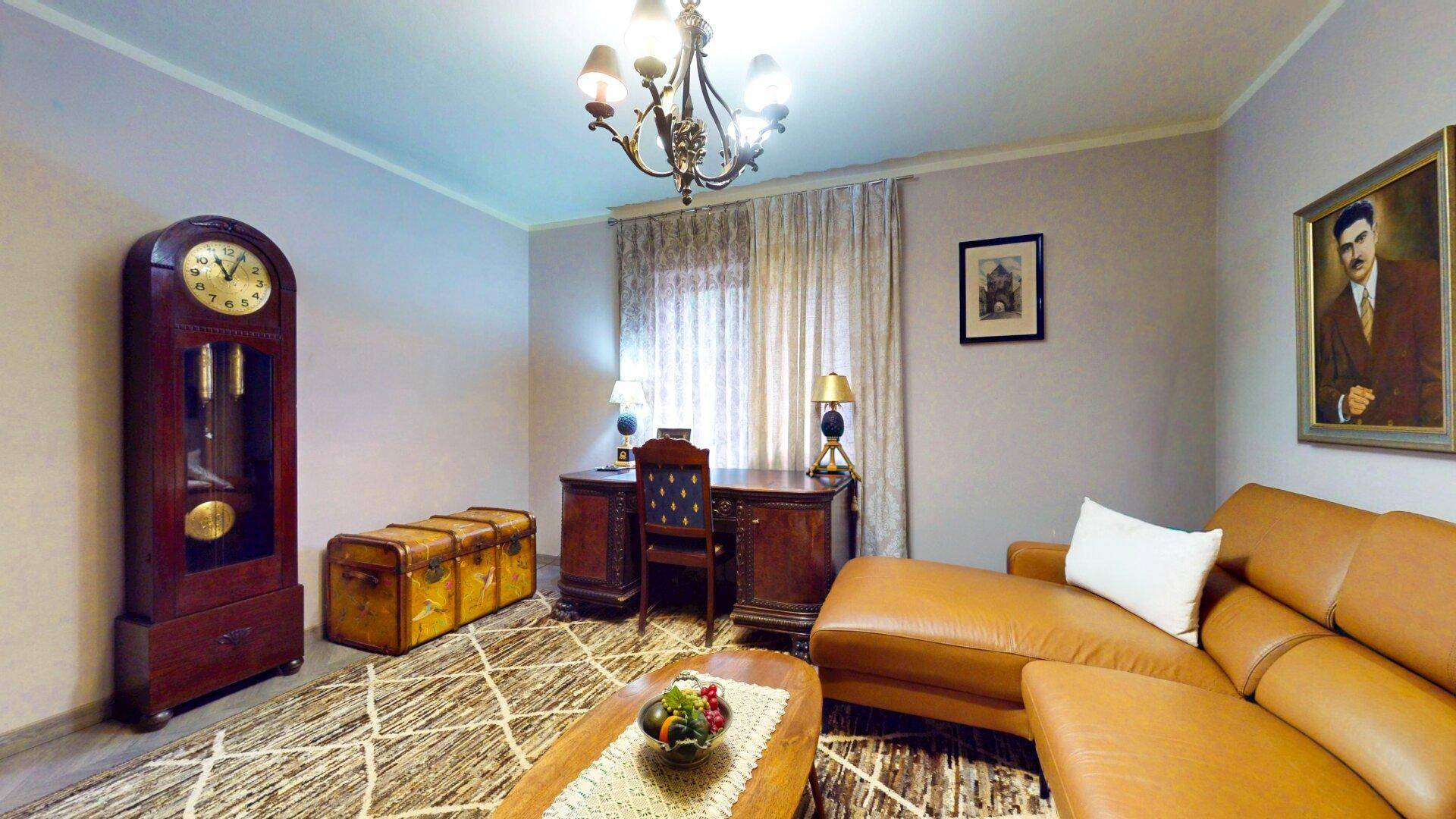 Gemütliches Wohnzimmer mit klassischem Schreibtisch, Ledersofa und Standuhr.