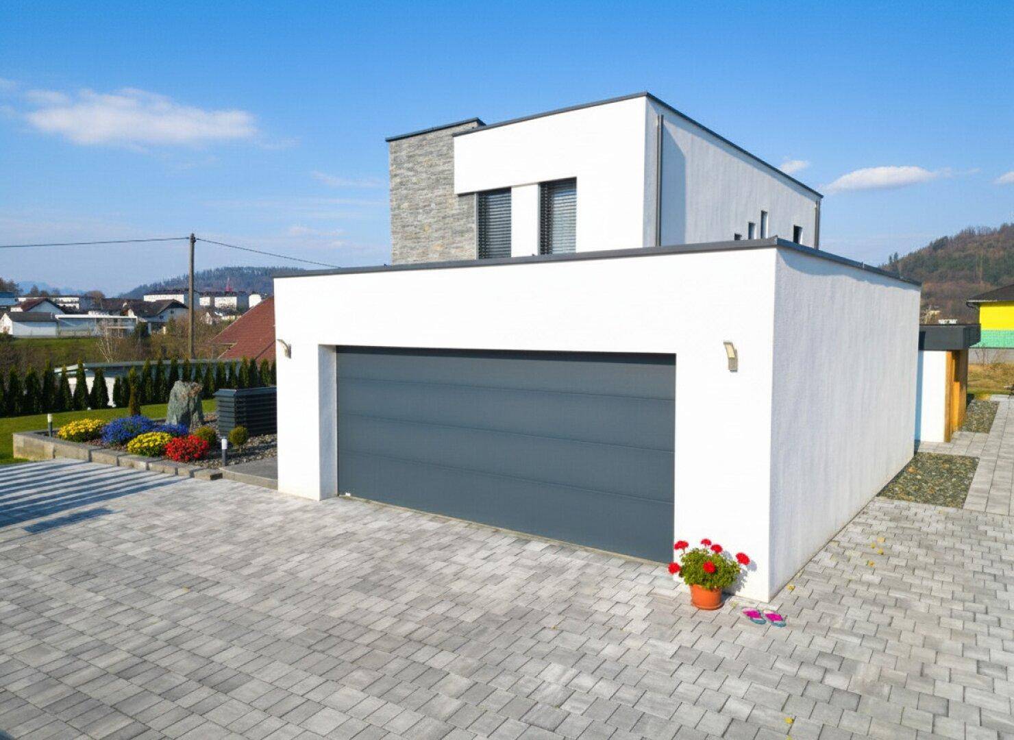 Moderne Hausfassade mit integrierter Doppelgarage und gepflasterter Einfahrt.
