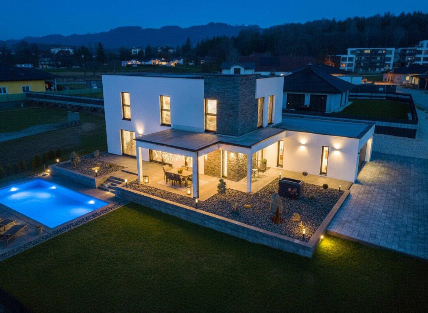 Beeindruckende Nachtansicht des modernen Hauses mit beleuchtetem Pool und Garten.