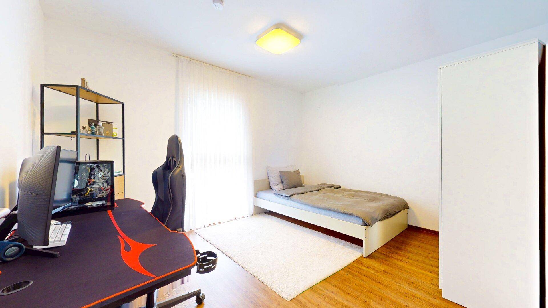 Freundliches Zimmer mit Einzelbett, Schreibtisch und großem Fenster.