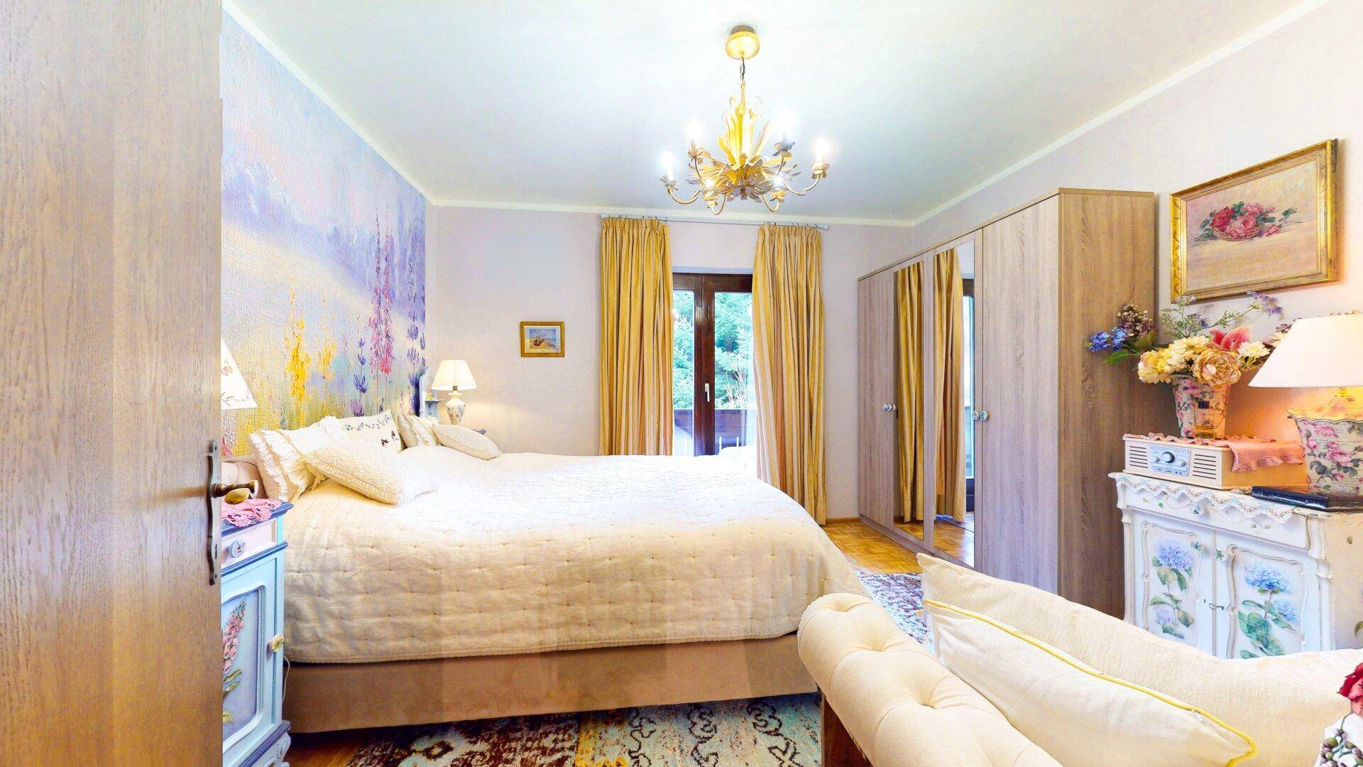 Helles Schlafzimmer mit großem Bett, Kleiderschrank und floraler Wandgestaltung.