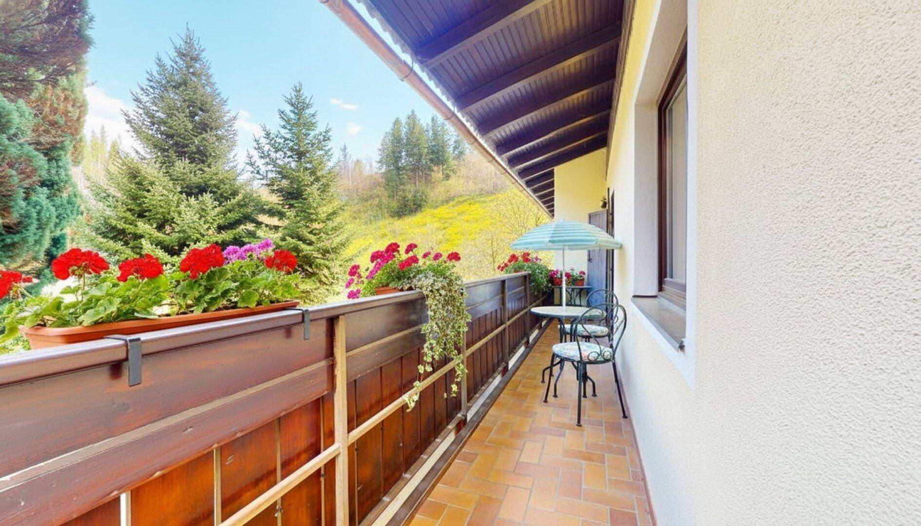 Sonniger Balkon mit kleinem Tisch, Stühlen und bunten Blumenkästen mit Bergblick.