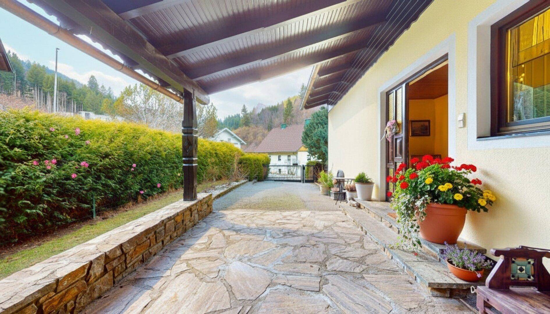 Überdachter Eingangsbereich mit Steinplatten und Blumenkübeln neben dem Haus.