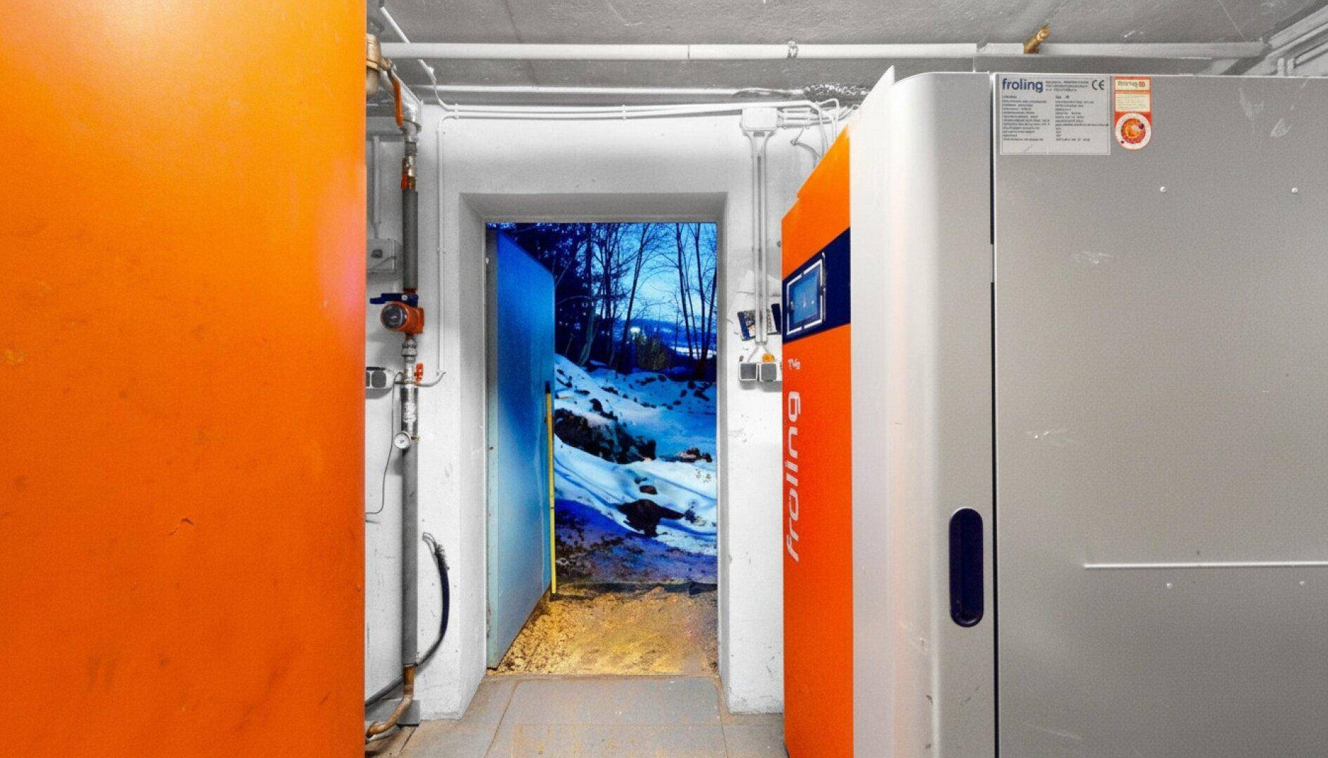 Heizraum mit moderner Heizanlage und einer Tür, die einen Blick auf eine winterliche Landschaft freigibt.