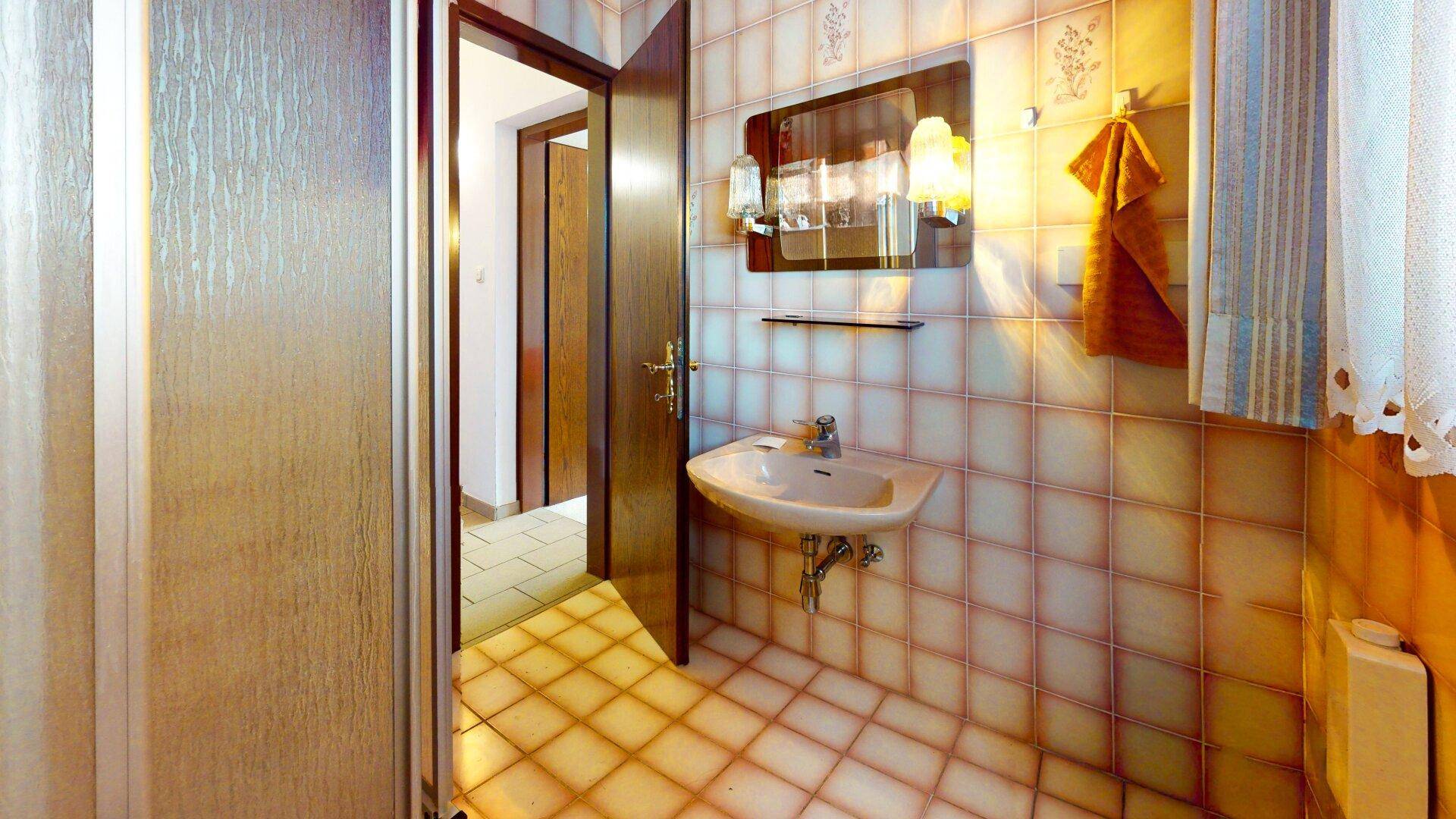 Badezimmer mit Waschbecken und Duschbereich, gekennzeichnet durch gemusterte Fliesen an Wänden und Boden.