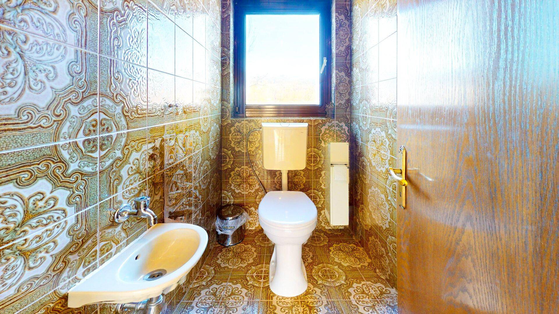 Badezimmer mit Toilette, Bidet und Fenster, verziert mit auffälligen gemusterten Fliesen.