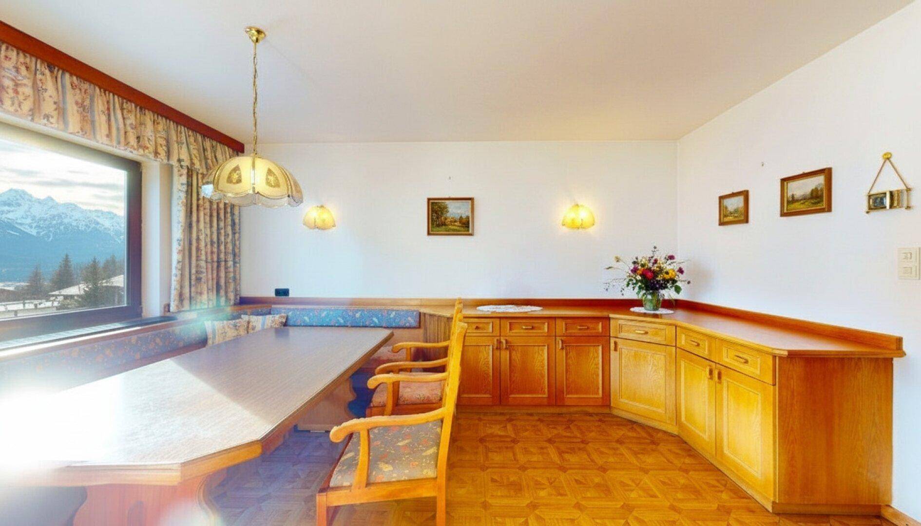 Heller Essbereich mit großem Holztisch, Eckbank und Schränken, bietet einen schönen Bergblick.