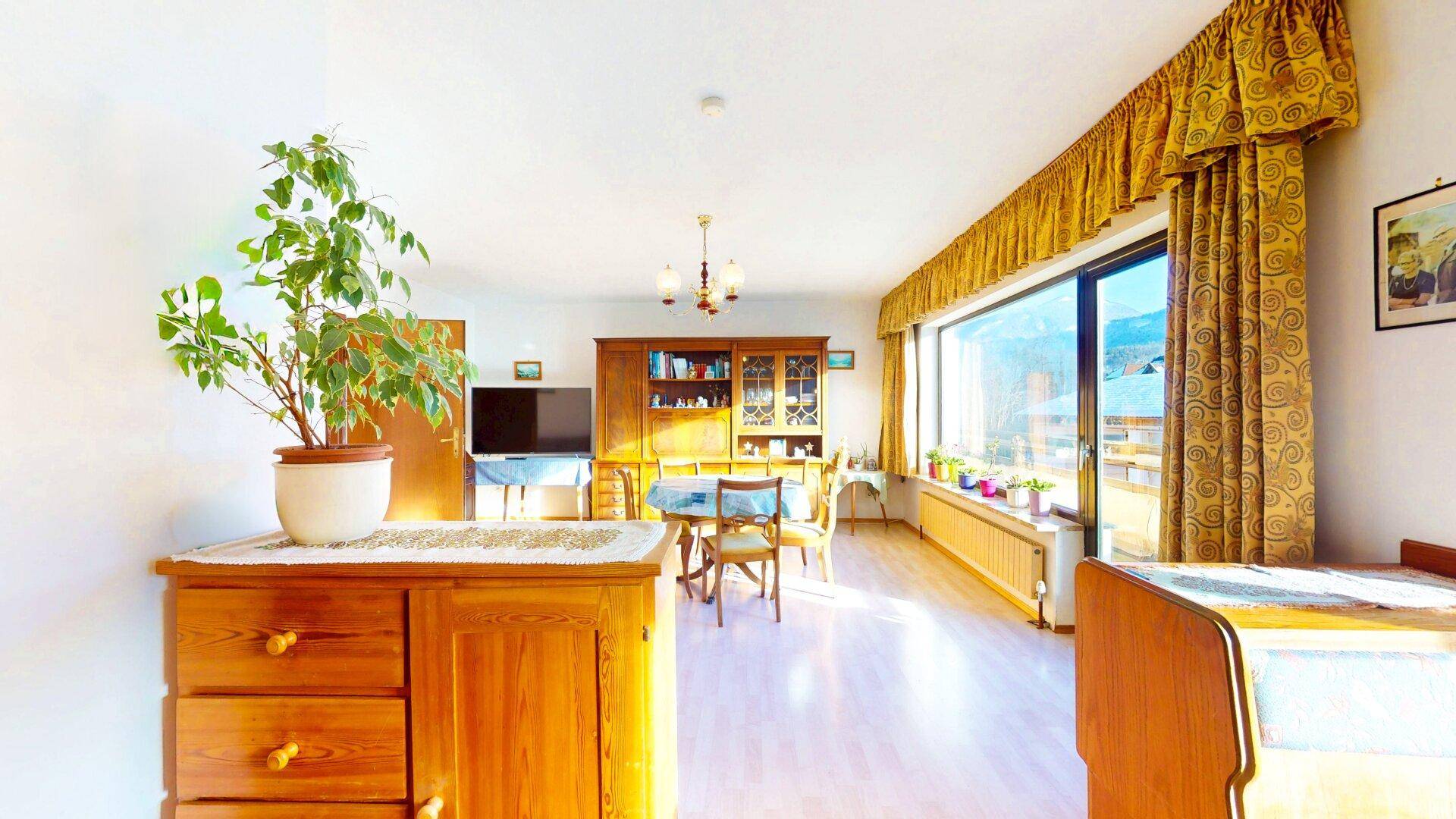 Geräumiges Wohnzimmer mit Holzmöbeln, Esstisch und großem Fenster, das viel Licht hereinlässt.