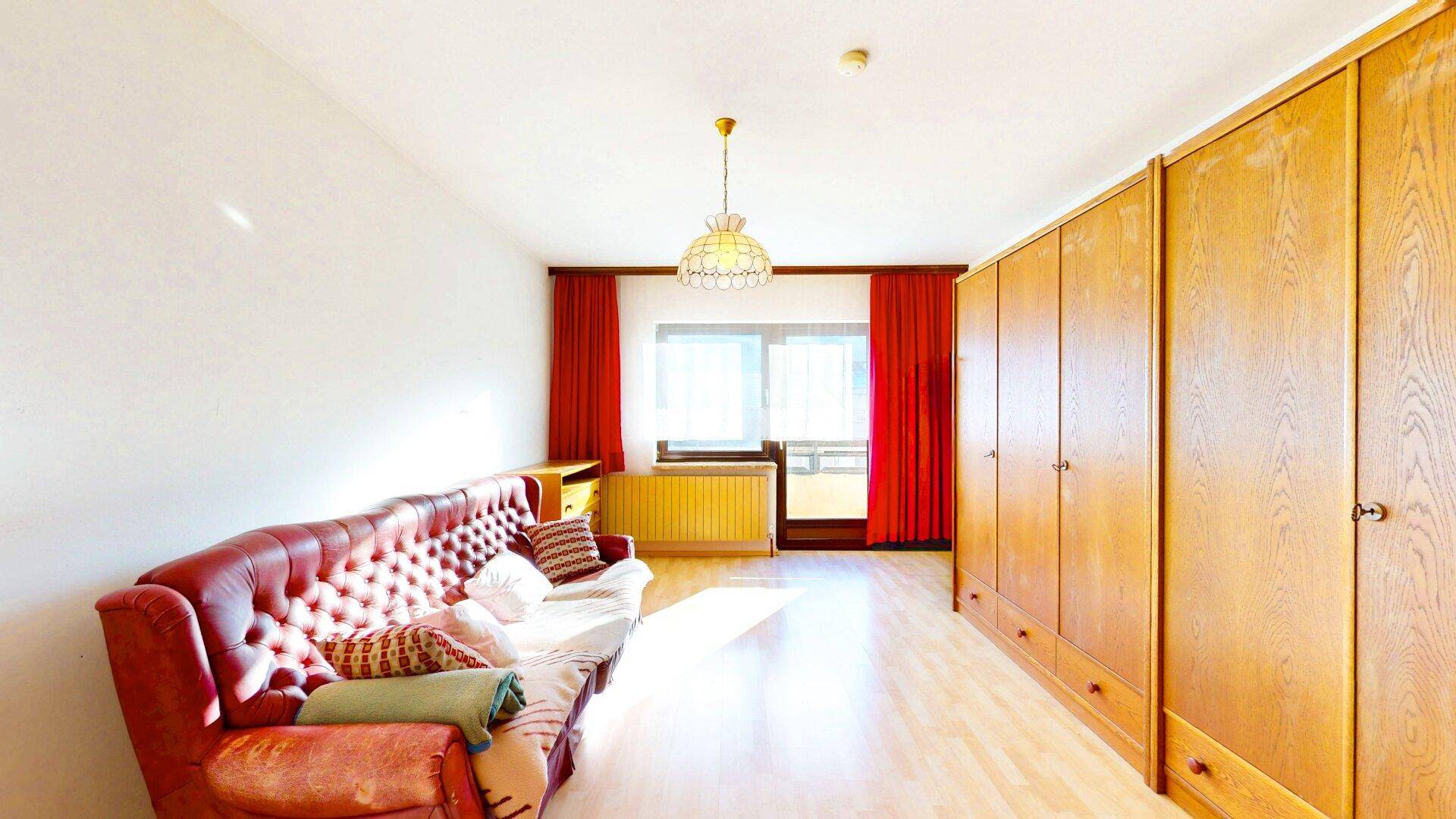 Wohnzimmer mit rotem Sofa, Holzschränken und Fenster mit roten Vorhängen auf Laminatboden.