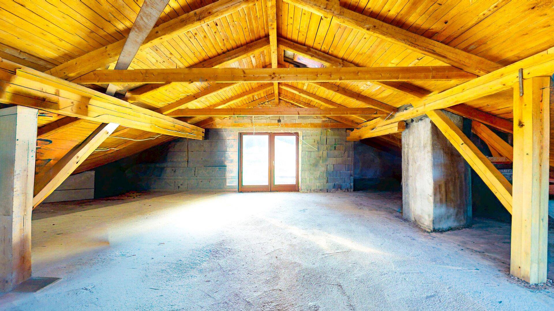 Unausgebauter Dachboden mit sichtbaren Holzbalken und Betonboden, bietet Ausbaupotenzial.