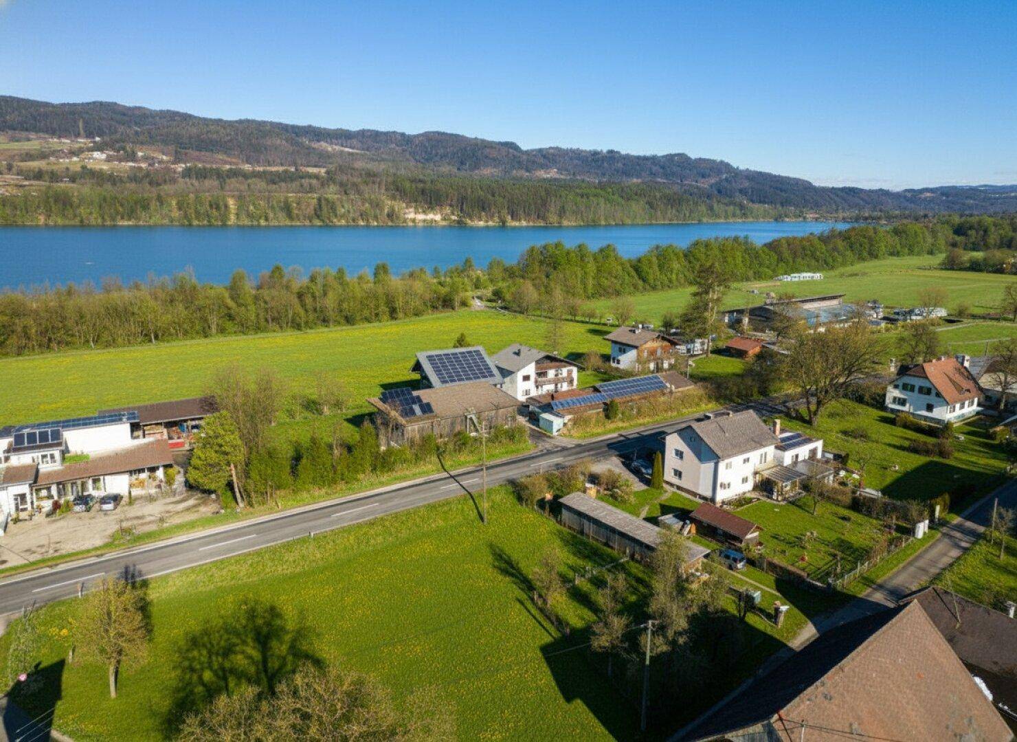 Luftaufnahme einer Straße entlang eines Sees, umgeben von Häusern und grünen Landschaften.