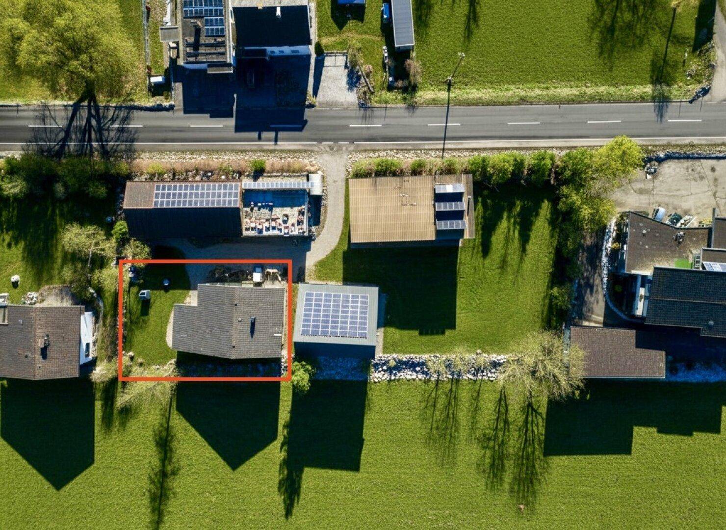 Vogelperspektive eines Hauses mit Solaranlagen auf dem Dach, umgeben von einer grünen Rasenfläche.