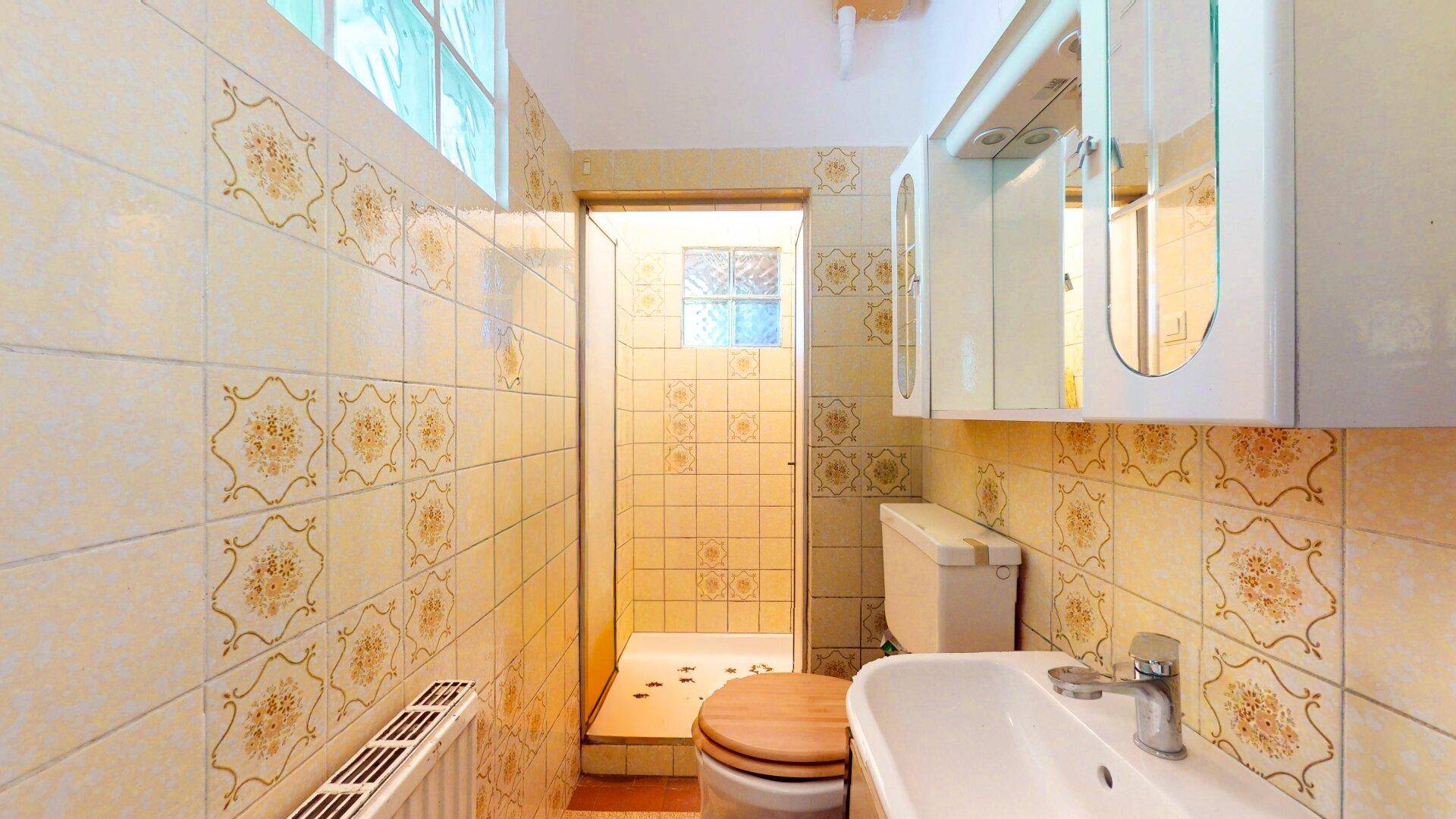 Badezimmer mit gelblichen Fliesen, Duschkabine, WC und Waschbecken, typisch für die 80er Jahre.