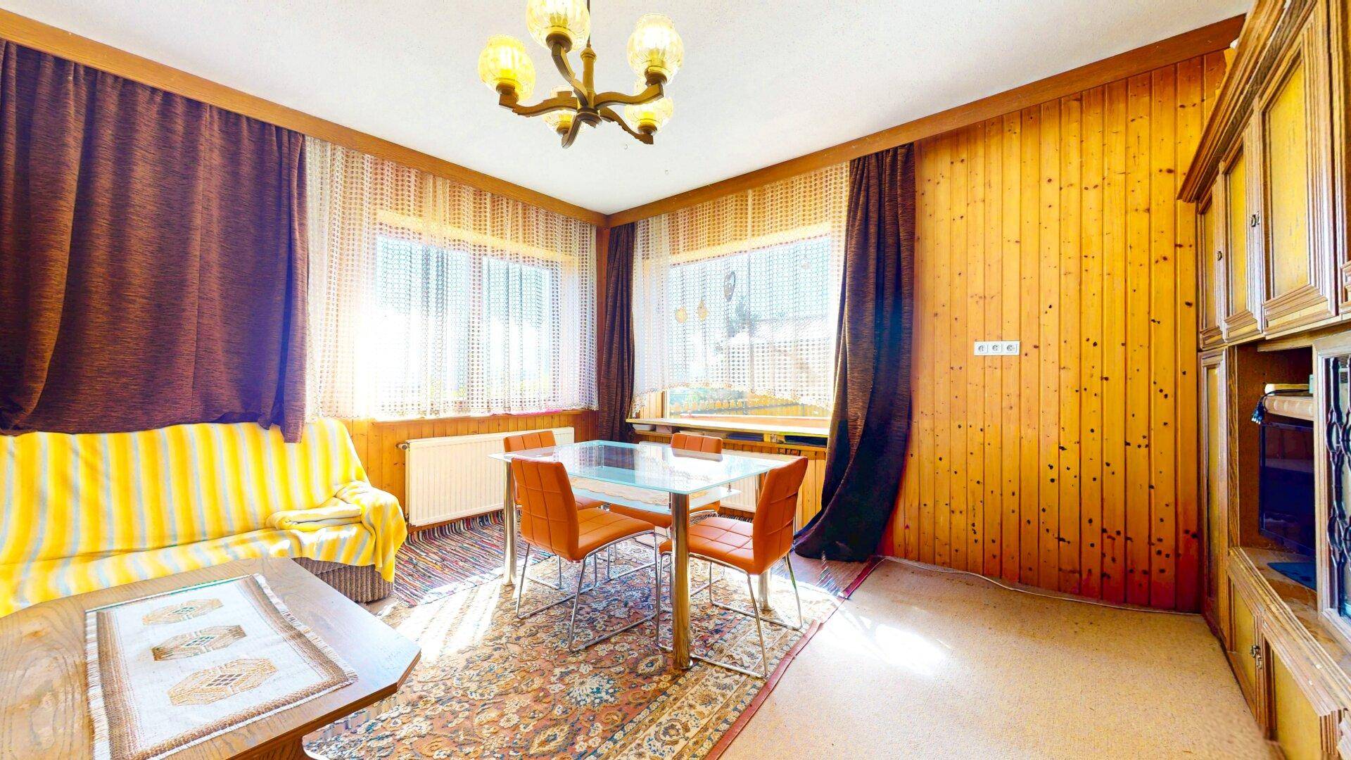 Wohn- und Essbereich mit Holzvertäfelung, Sofa und Esstisch, durchflutet von natürlichem Licht.