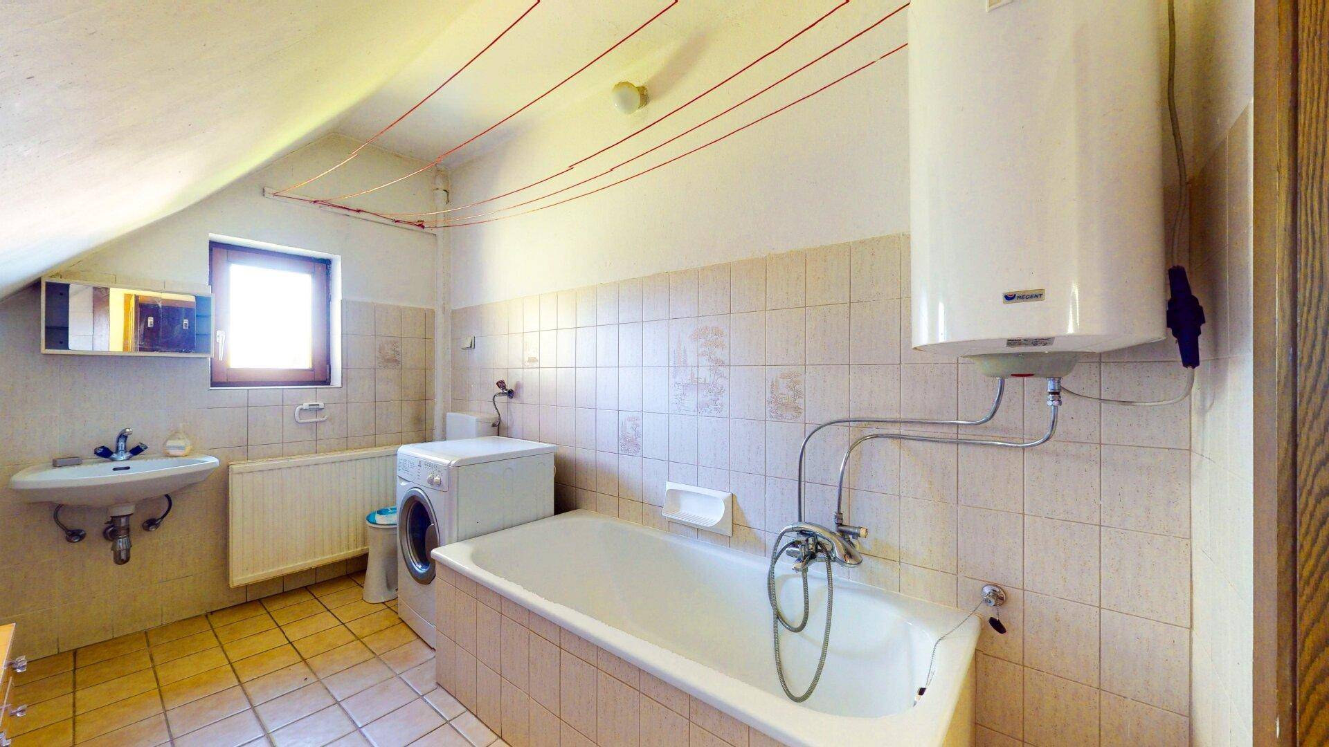 Dachgeschoss-Badezimmer mit Badewanne, Waschbecken, Waschmaschine und Warmwasserboiler.