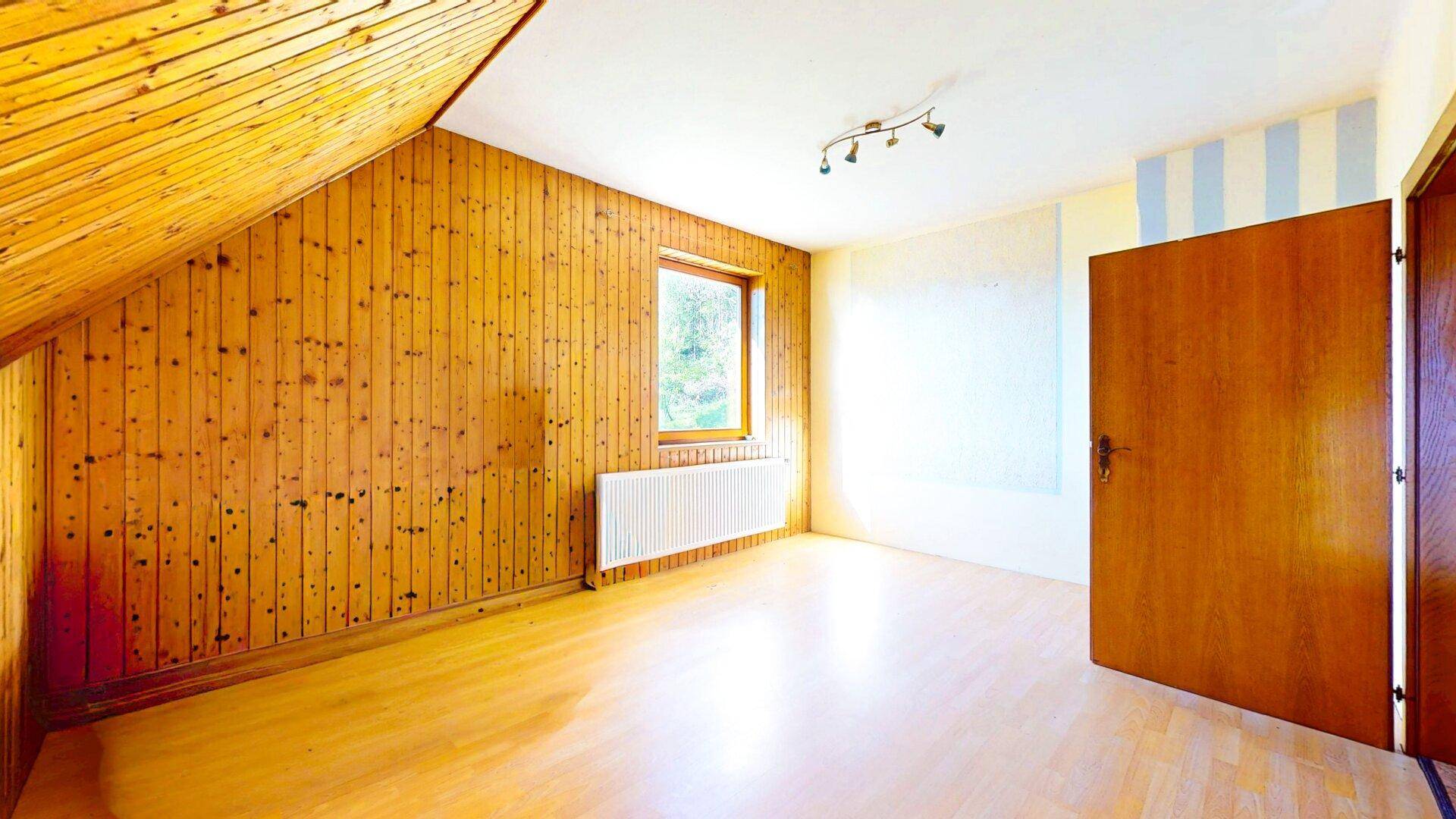 Dachgeschossraum mit Holzvertäfelung, schrägen Wänden und einem Fenster.
