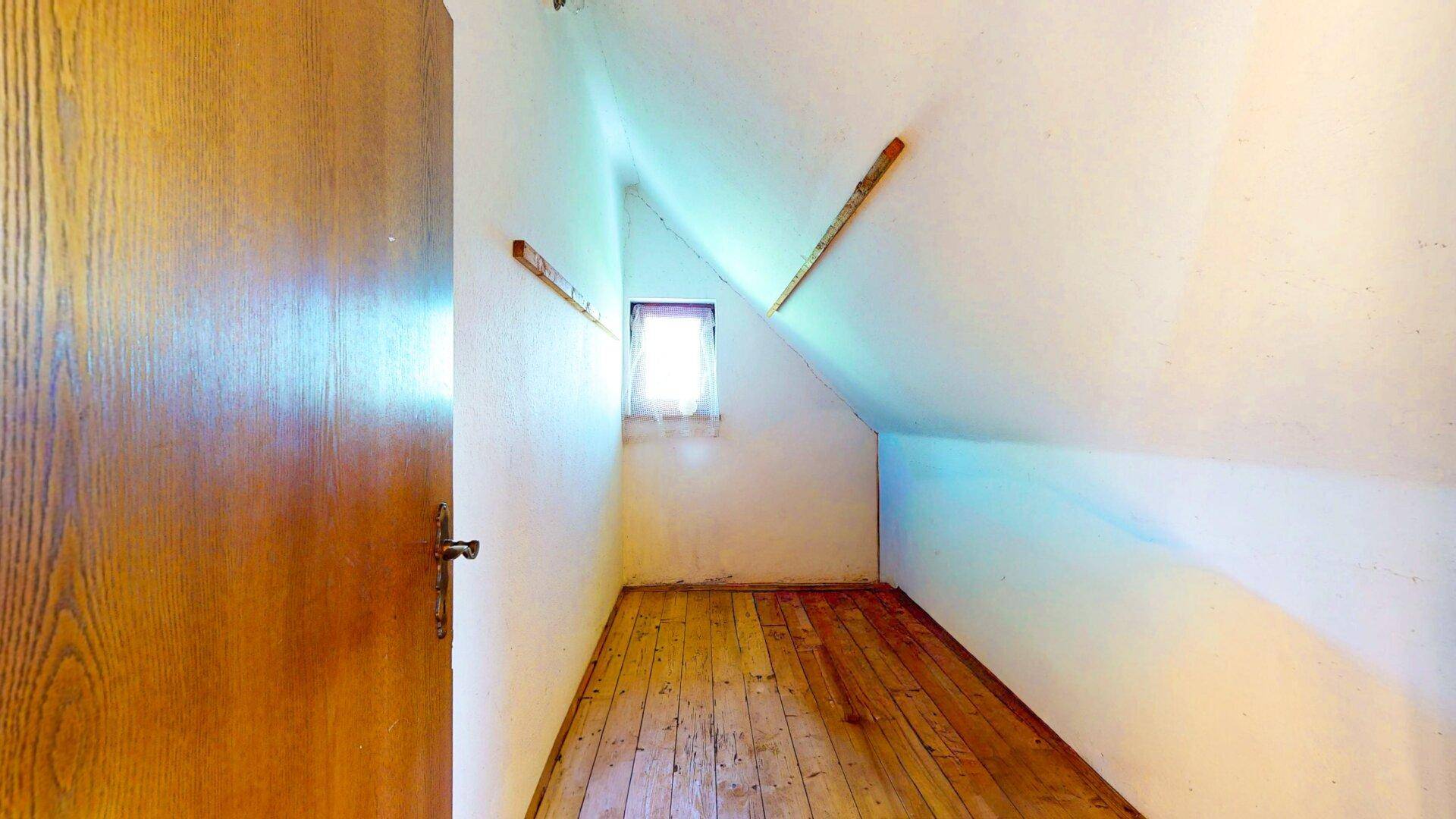 Kleiner Abstellraum im Dachgeschoss mit schrägen Wänden und einem kleinen Fenster.