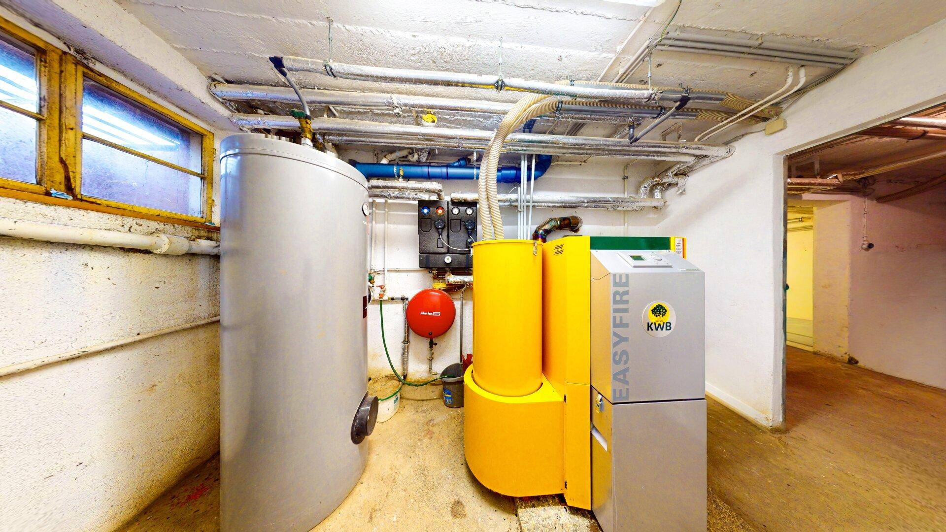 Kellerraum mit Heizungsanlage, Warmwasserspeicher und sichtbaren Rohrleitungen.