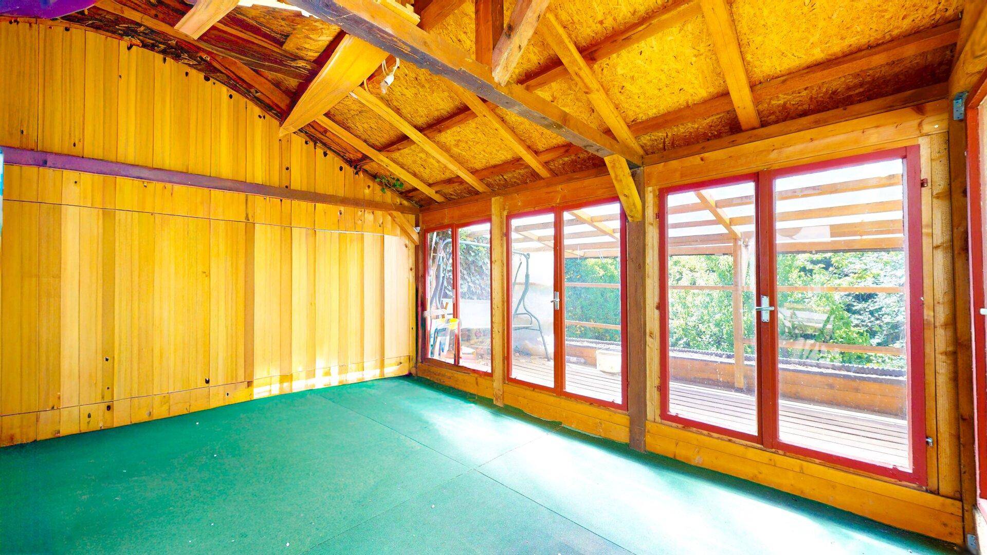 Heller Wintergarten mit Holzverkleidung und großen Fenstern, die viel Licht hereinlassen.