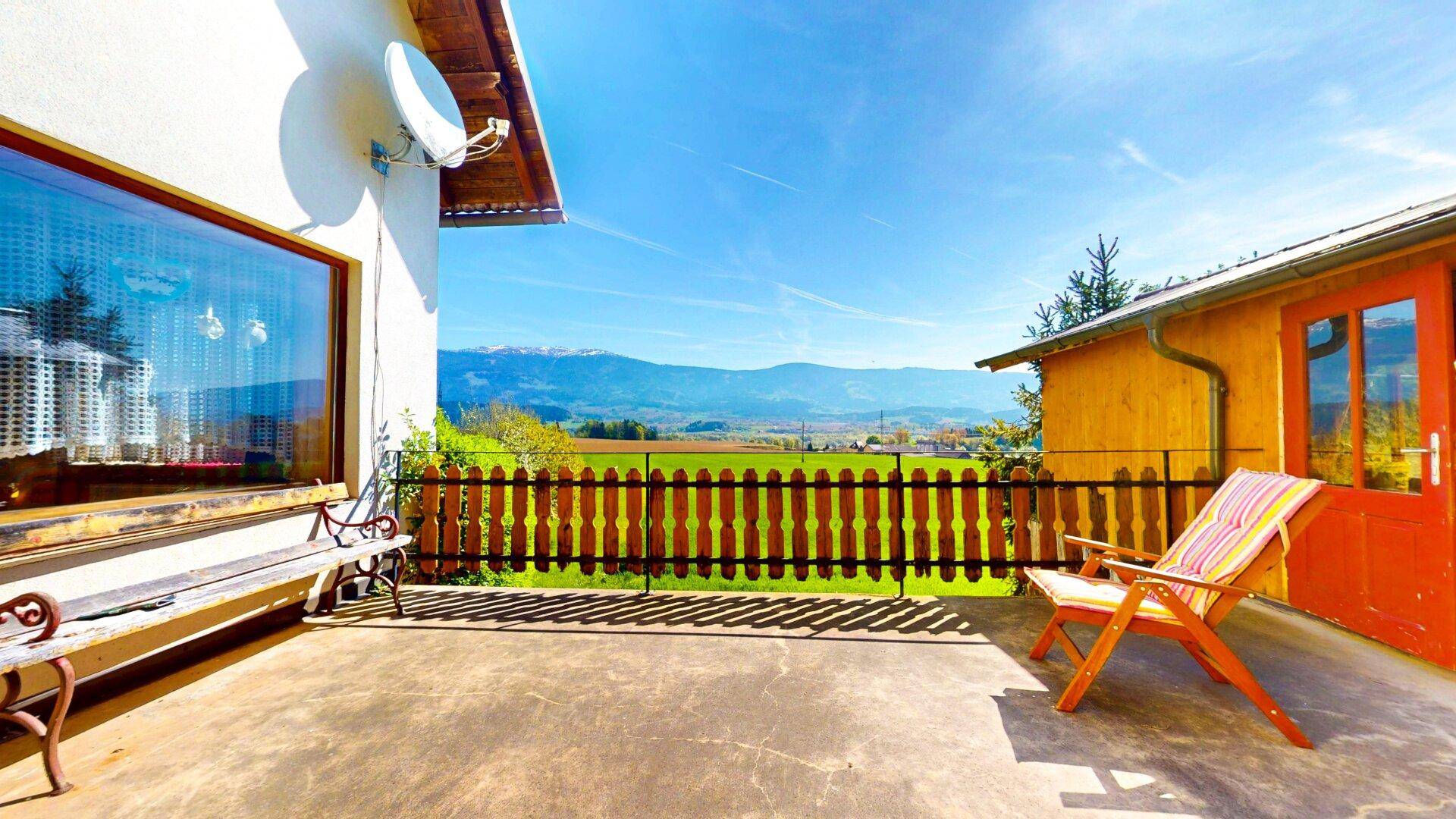 Sonniger Terrassenbereich mit Bergblick, Holzzaun und Sitzgelegenheiten zum Entspannen im Freien.