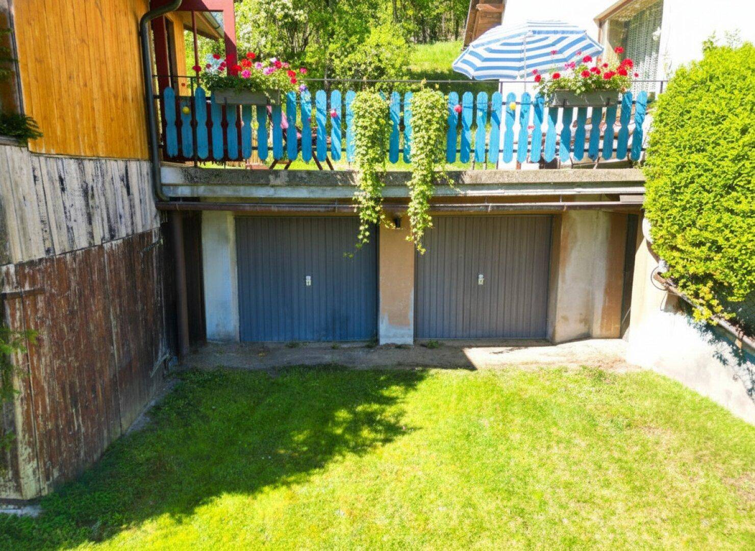 Zwei Garagen im Untergeschoss mit darüberliegendem Balkon und kleiner Rasenfläche.