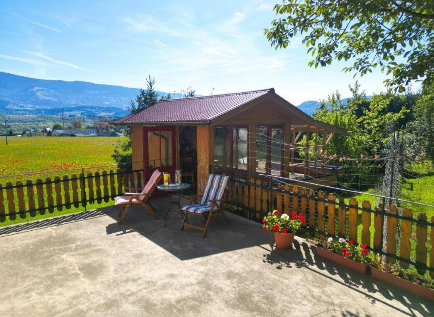Gemütliche Terrasse mit Gartenmöbeln und einem kleinen Holzhaus, umgeben von Natur und Bergblick.