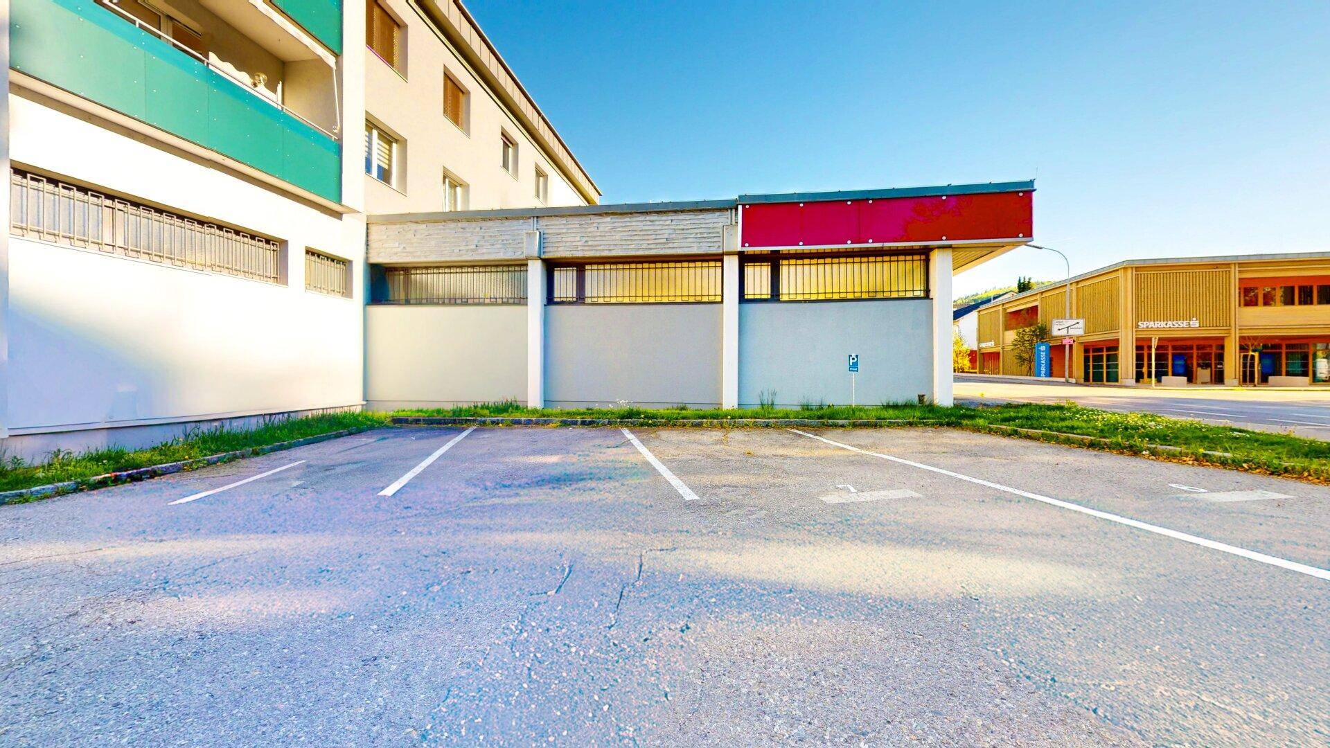 Außenansicht des Gewerbegebäudes vom Parkplatz aus, mit der Fassade und markierten Stellplätzen.
